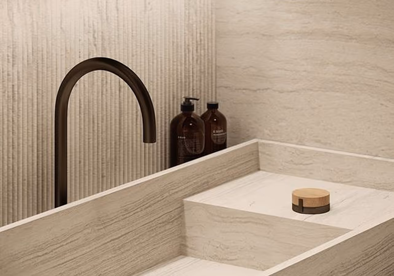 Minimalist beige stone sink with a curved dark faucet and two brown pump bottles in the background.