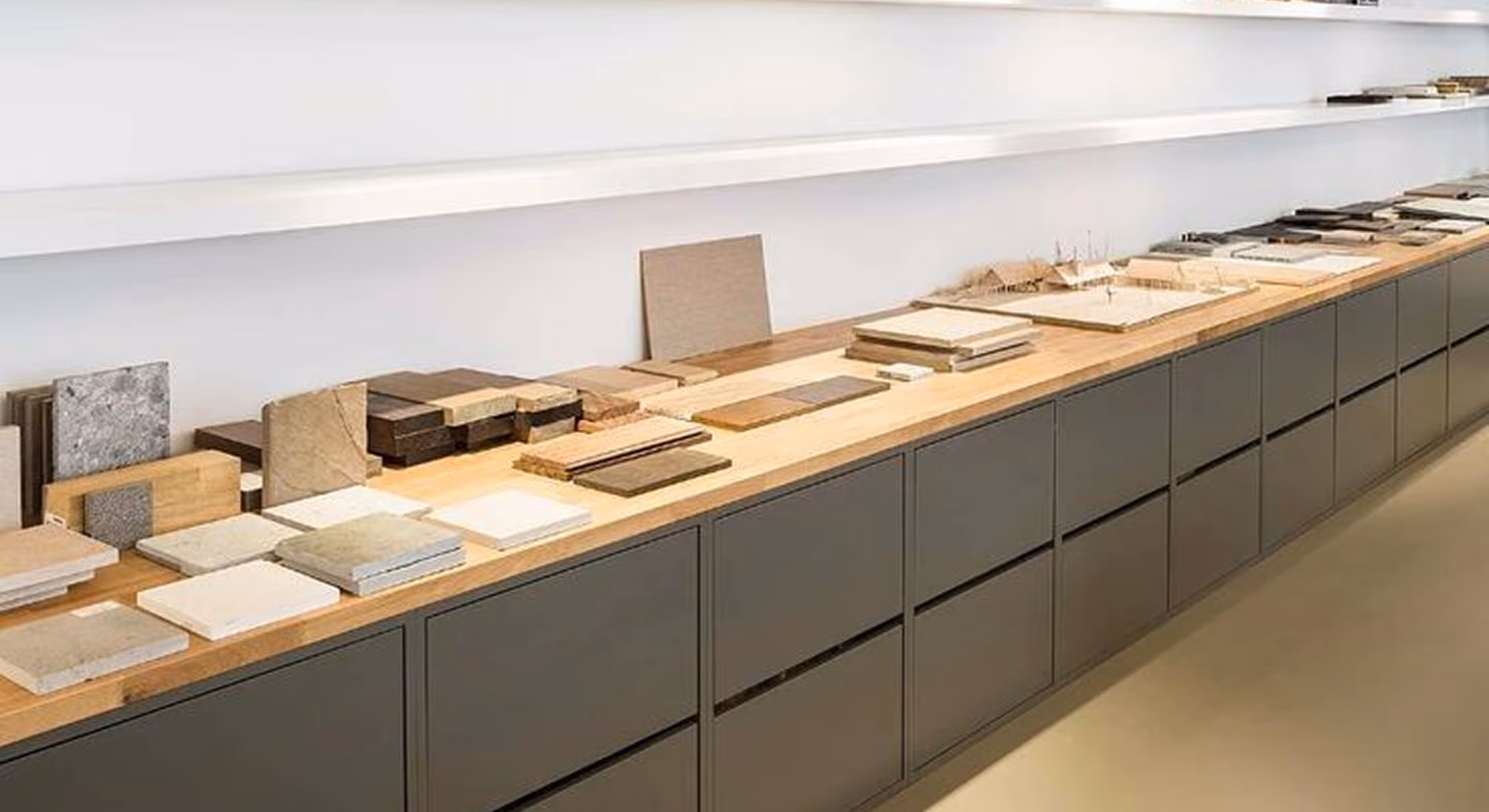 Long wooden table displaying various wood, stone, and tile samples in an interior showroom.