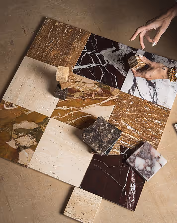 Hand arranging various marble and stone tile samples on a surface with different colors and patterns.