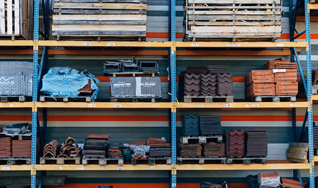 Shelves in warehouse stocked with various building materials like tiles and bricks on wooden pallets.