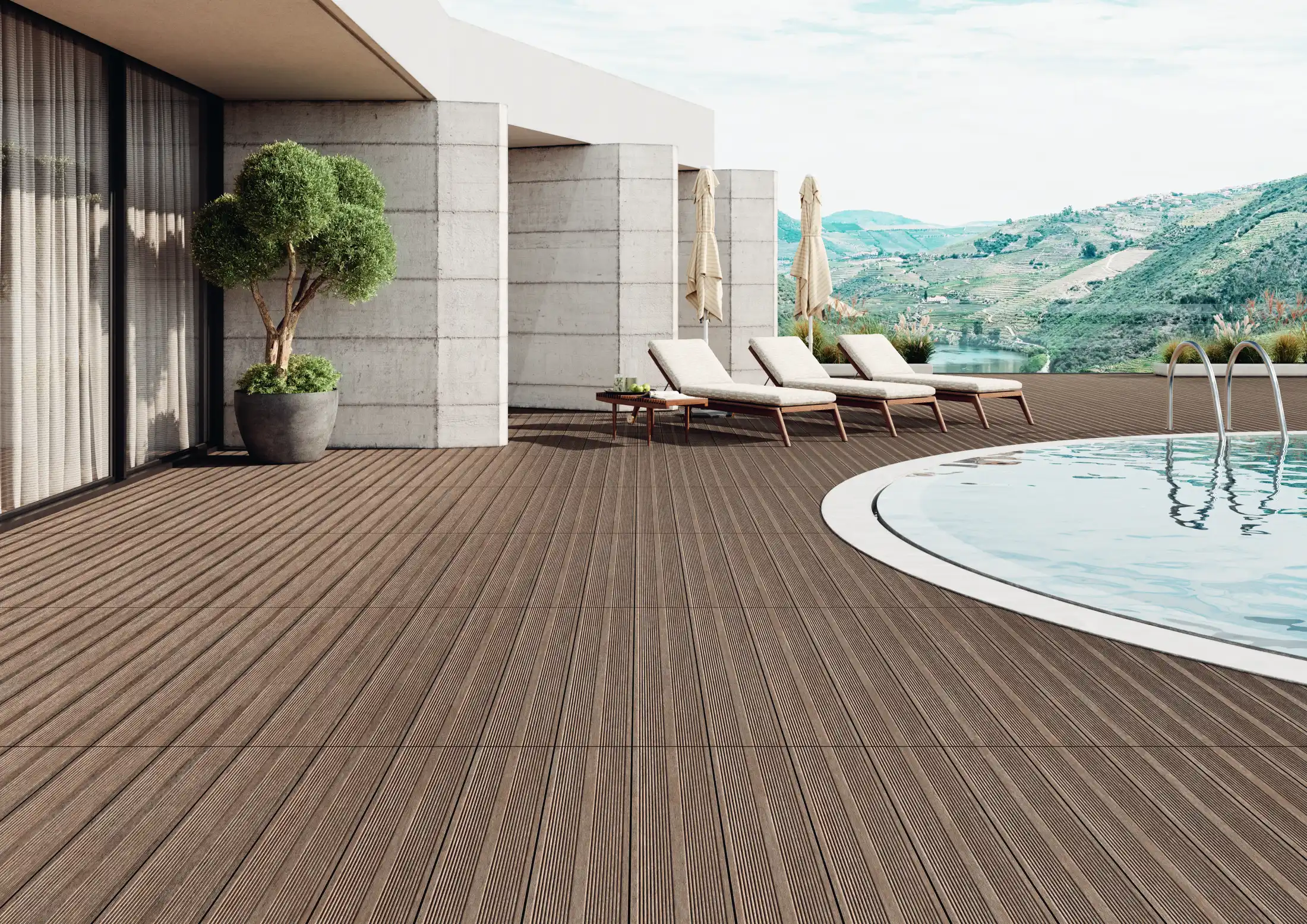 Modern outdoor pool area with brown deck flooring, lounge chairs, umbrellas, and mountain views.