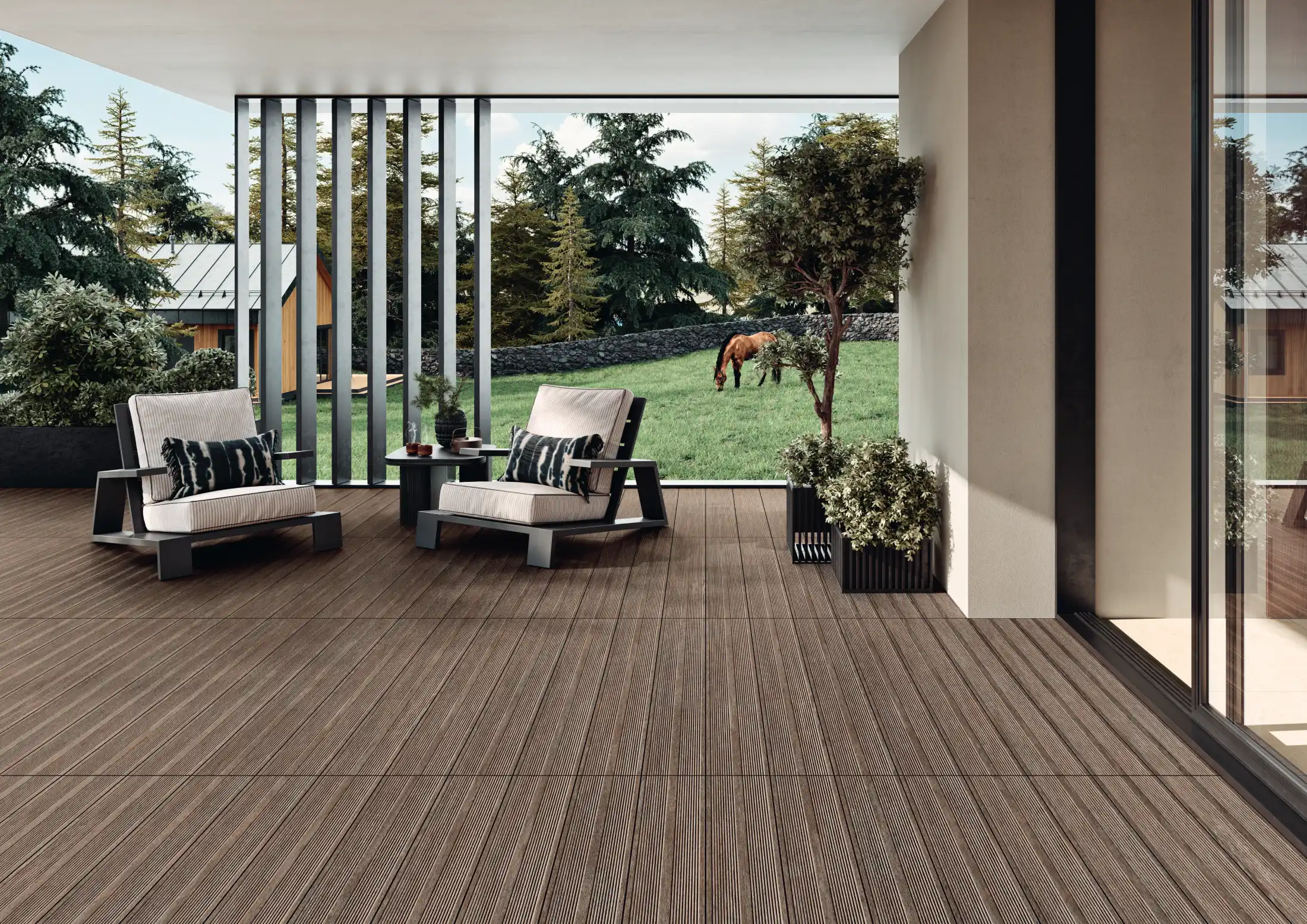 Modern patio with brown wood-grain deck flooring, two cushioned chairs, and green plants.