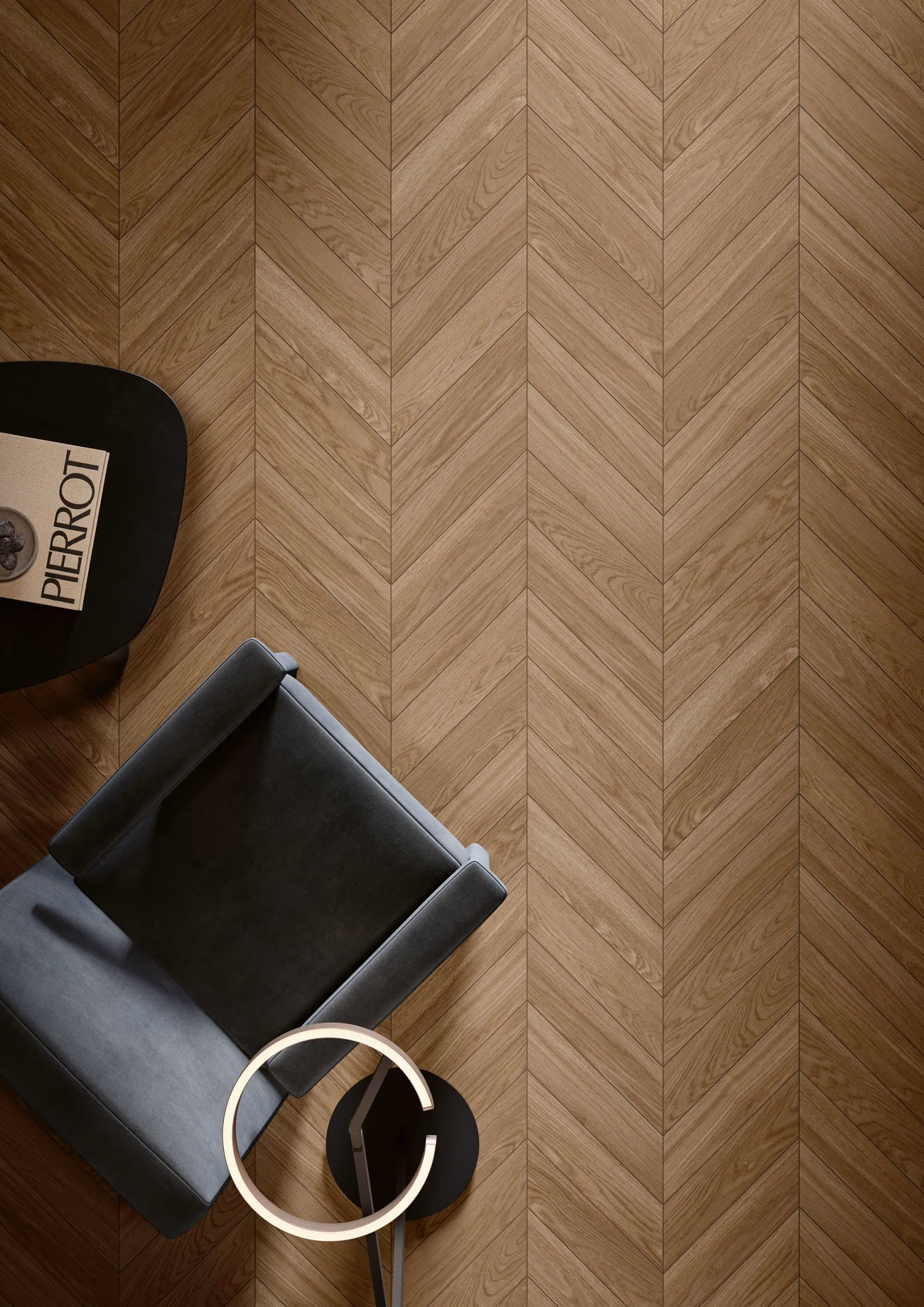 Top view of a gray armchair, modern lamp, and black table with a Pierrot book on chevron wood floor.