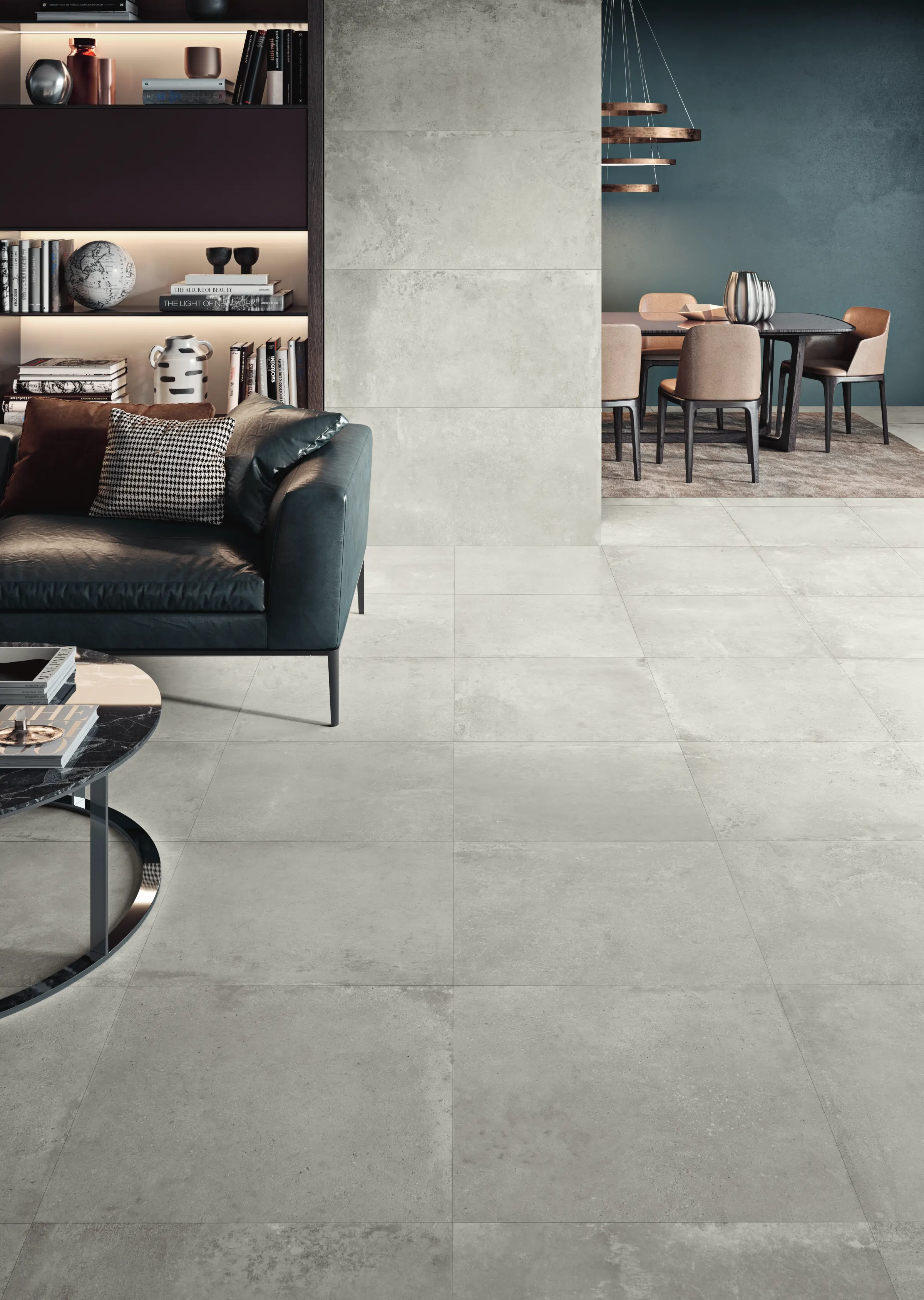 Modern living room with gray tiled floor, dark leather sofa, bookshelf, and dining area in background.