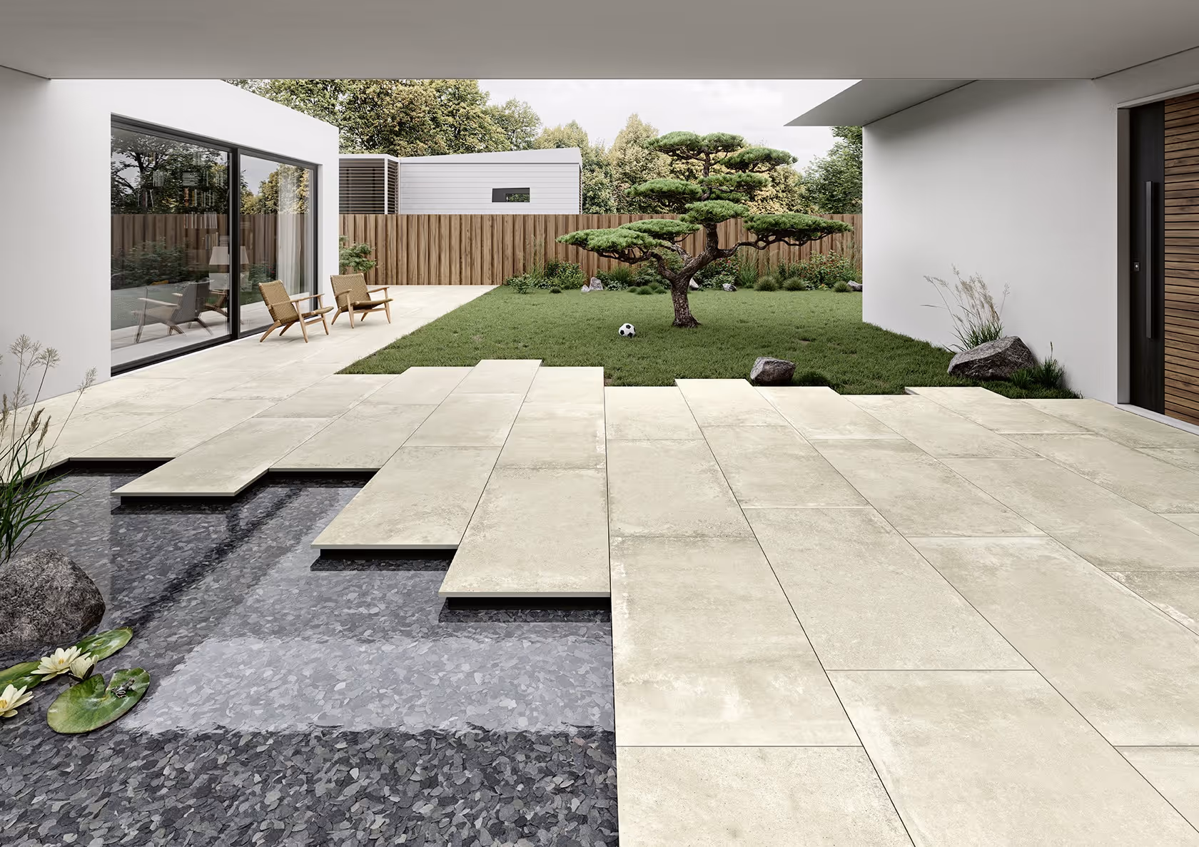 Modern patio with beige tiles extending over a reflecting pool, leading to a grassy yard with a bonsai tree.