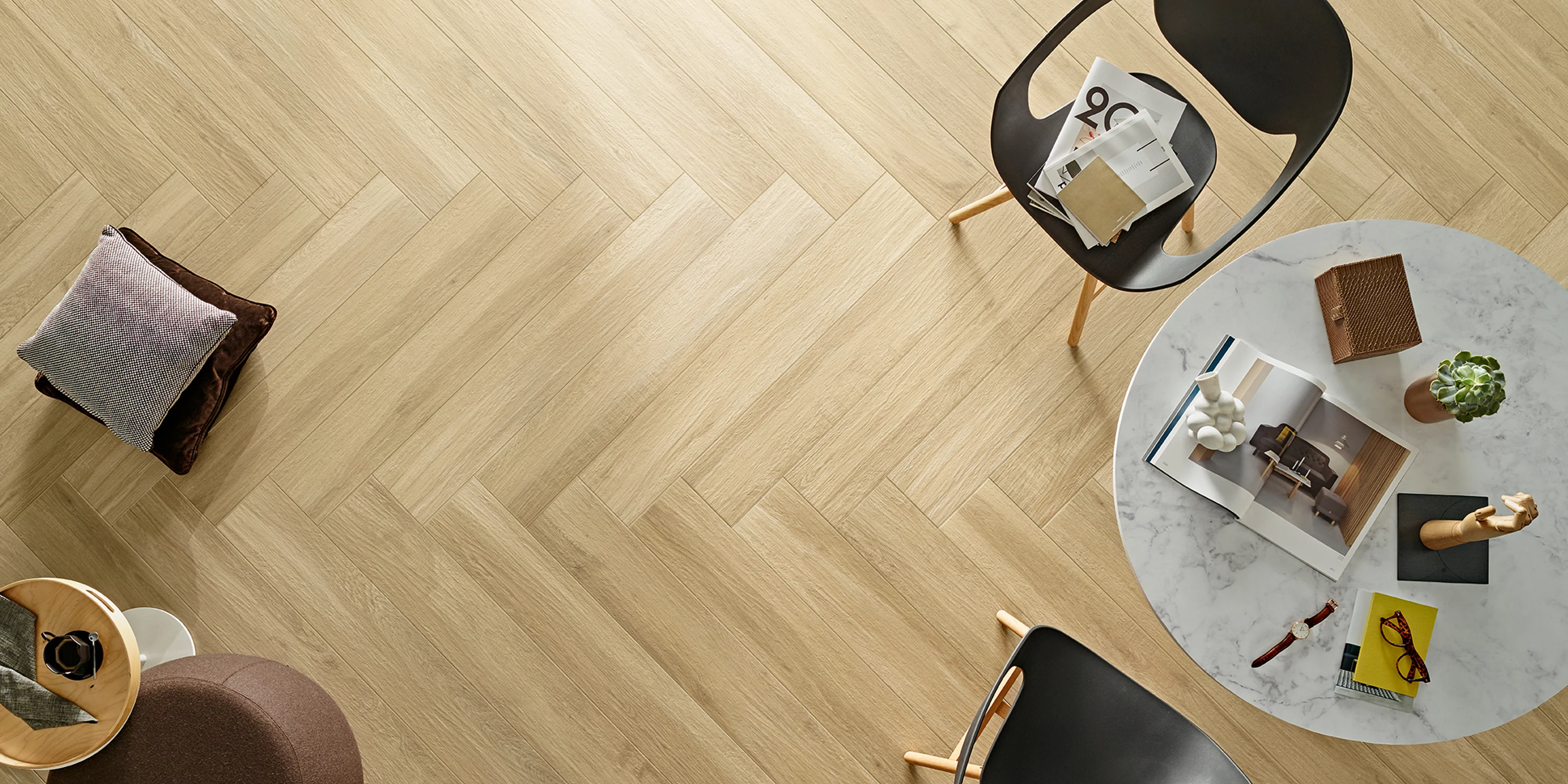 Top view of a light wood herringbone floor with chairs and a round marble table with decor items.