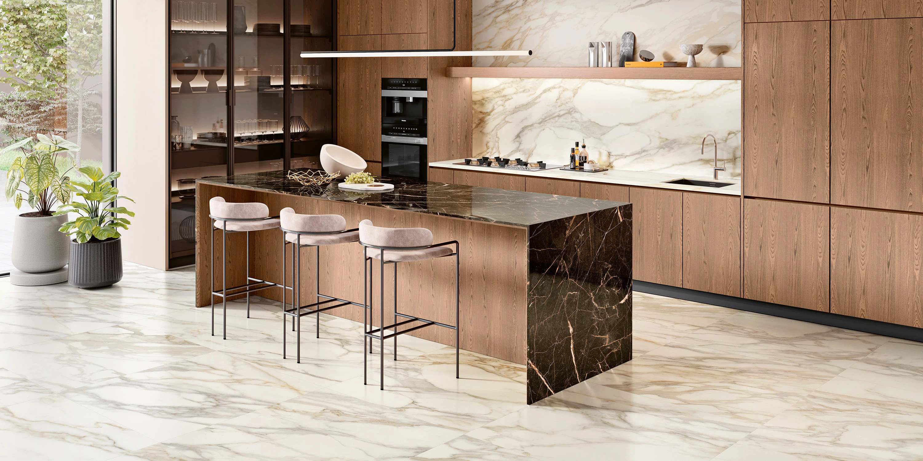 Modern kitchen with wood cabinets, marble floor, large island with black marble top, and three beige stools.