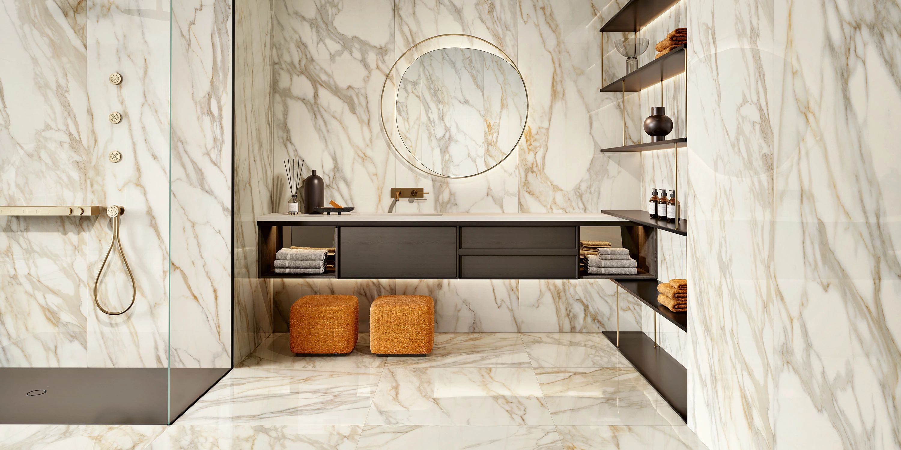 Modern bathroom with marble walls and floor, floating vanity, round lighted mirror, and orange stools.