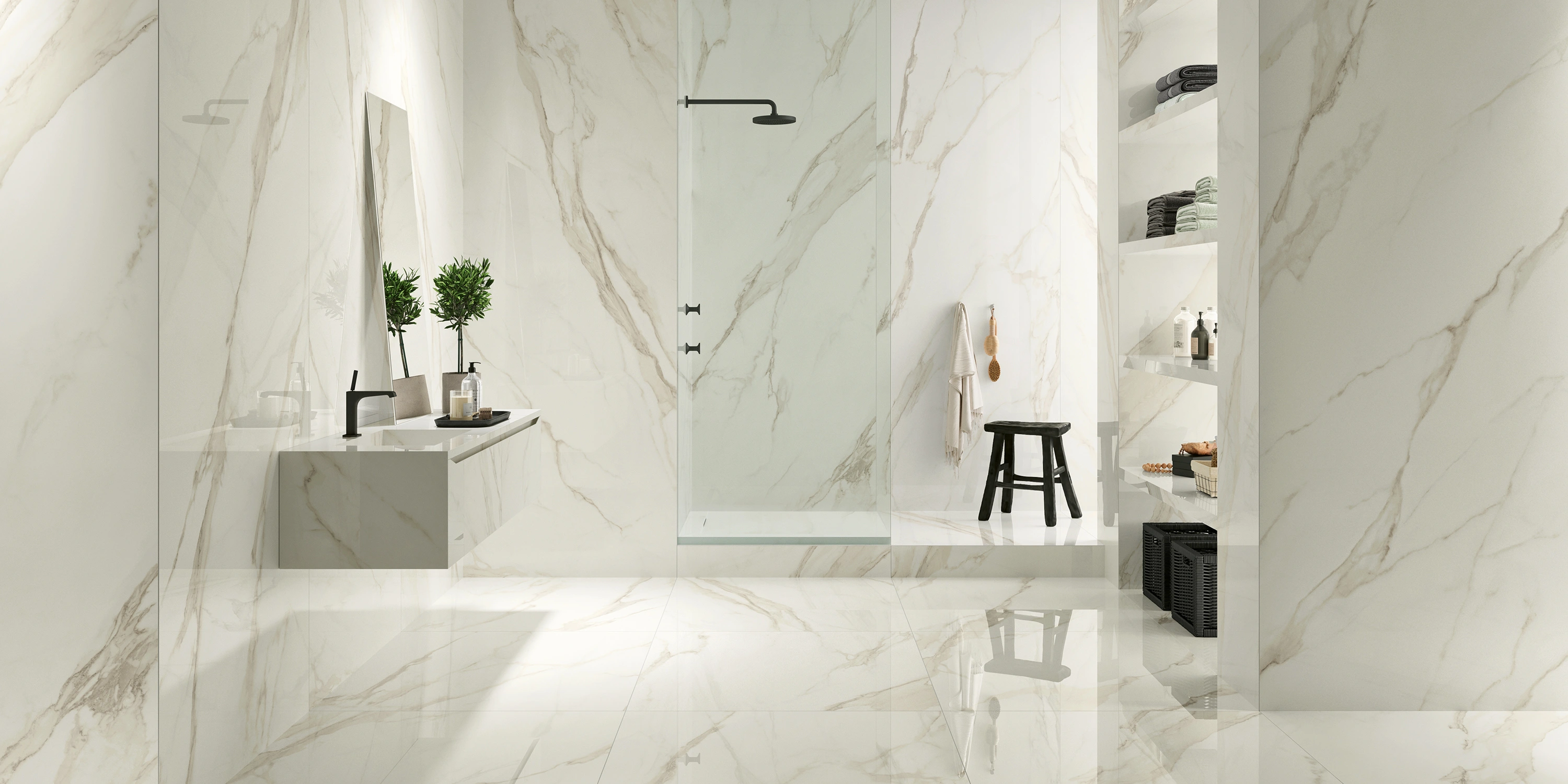 Modern bathroom with marble walls, floating sink, glass shower, black stool, and shelves with towels.