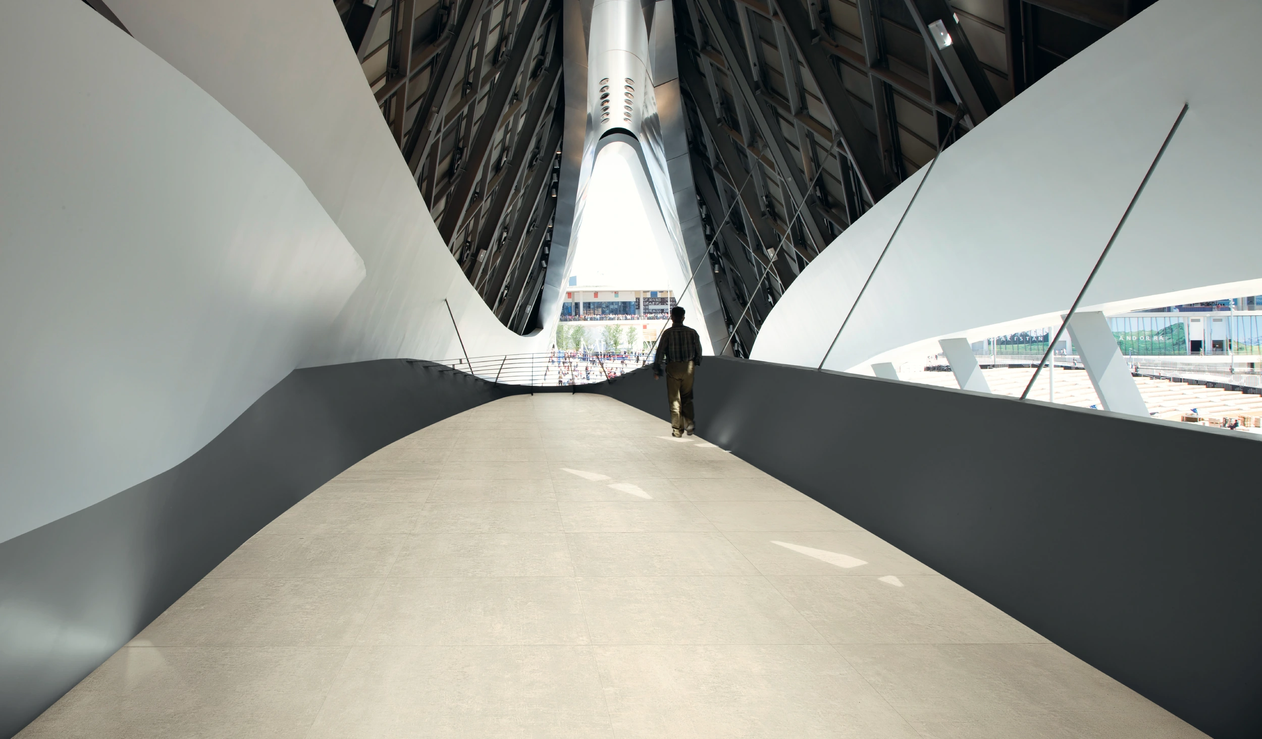 Person walking on a modern indoor bridge with curved white and black architectural walls.