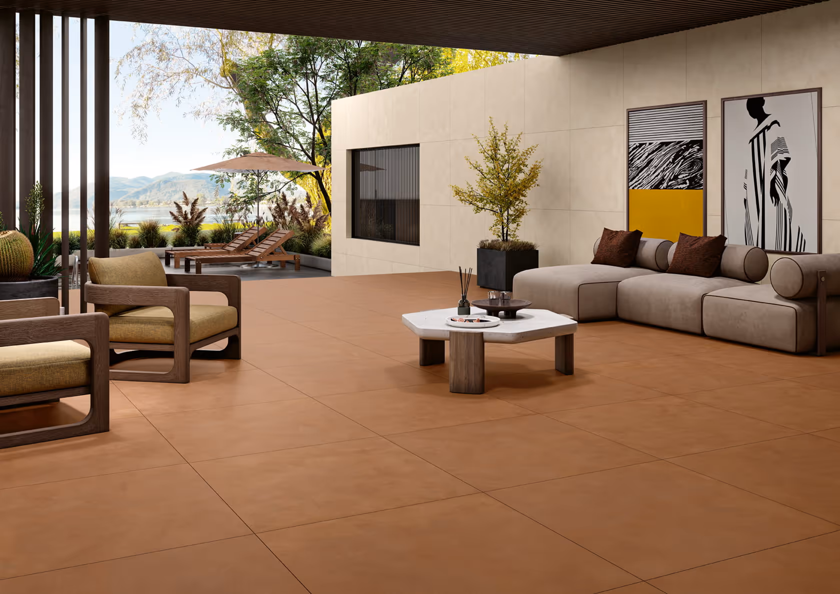 Modern outdoor patio with tan tiled floor, beige sofa, armchairs, table, plants, and lounge chairs under umbrella.