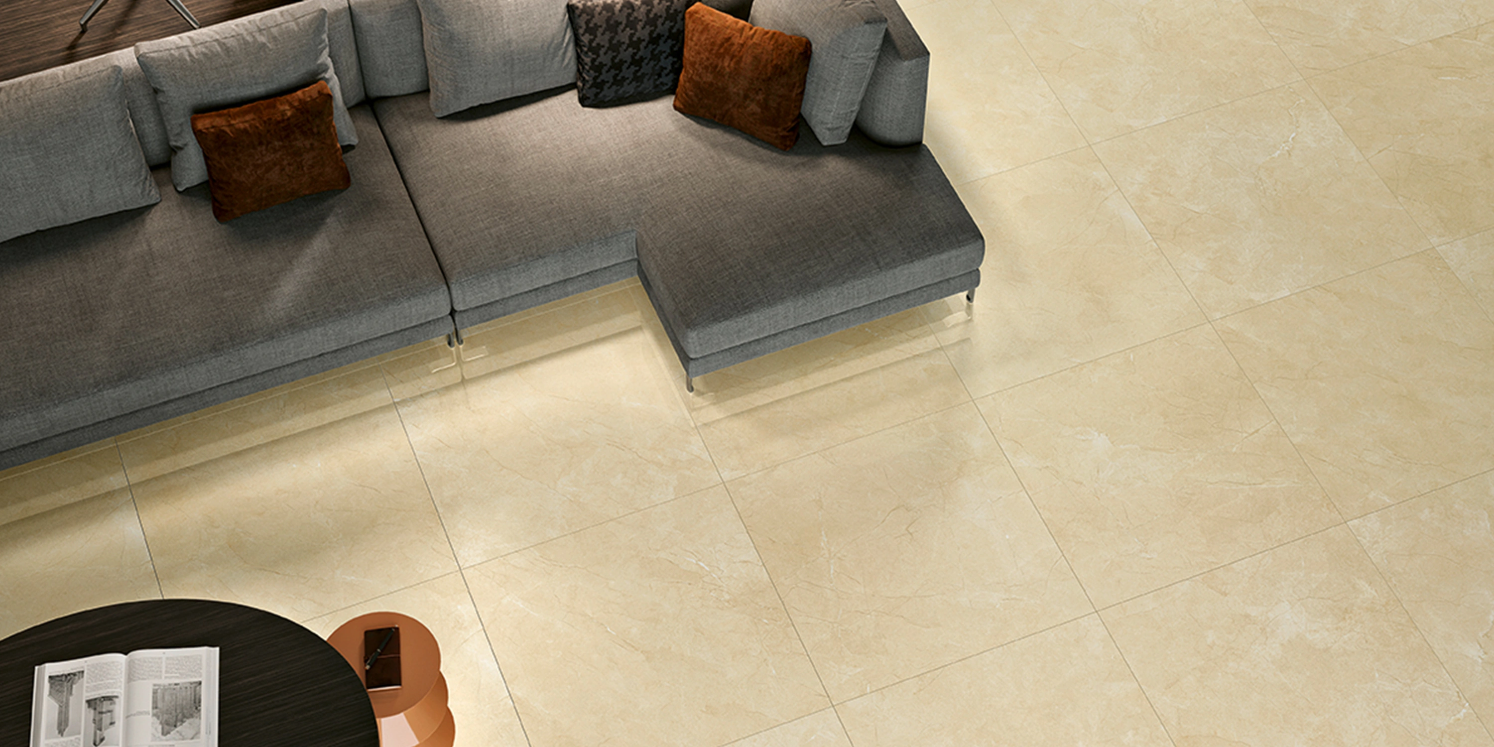 Top-down view of a gray sectional sofa with orange pillows on beige marble flooring.