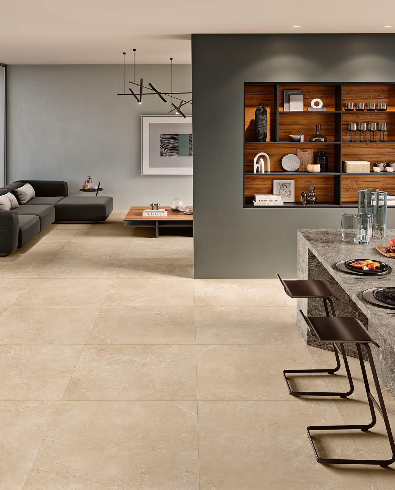 Modern living room with beige stone tile floor, gray sofa, wooden table, and kitchen island with bar stools.