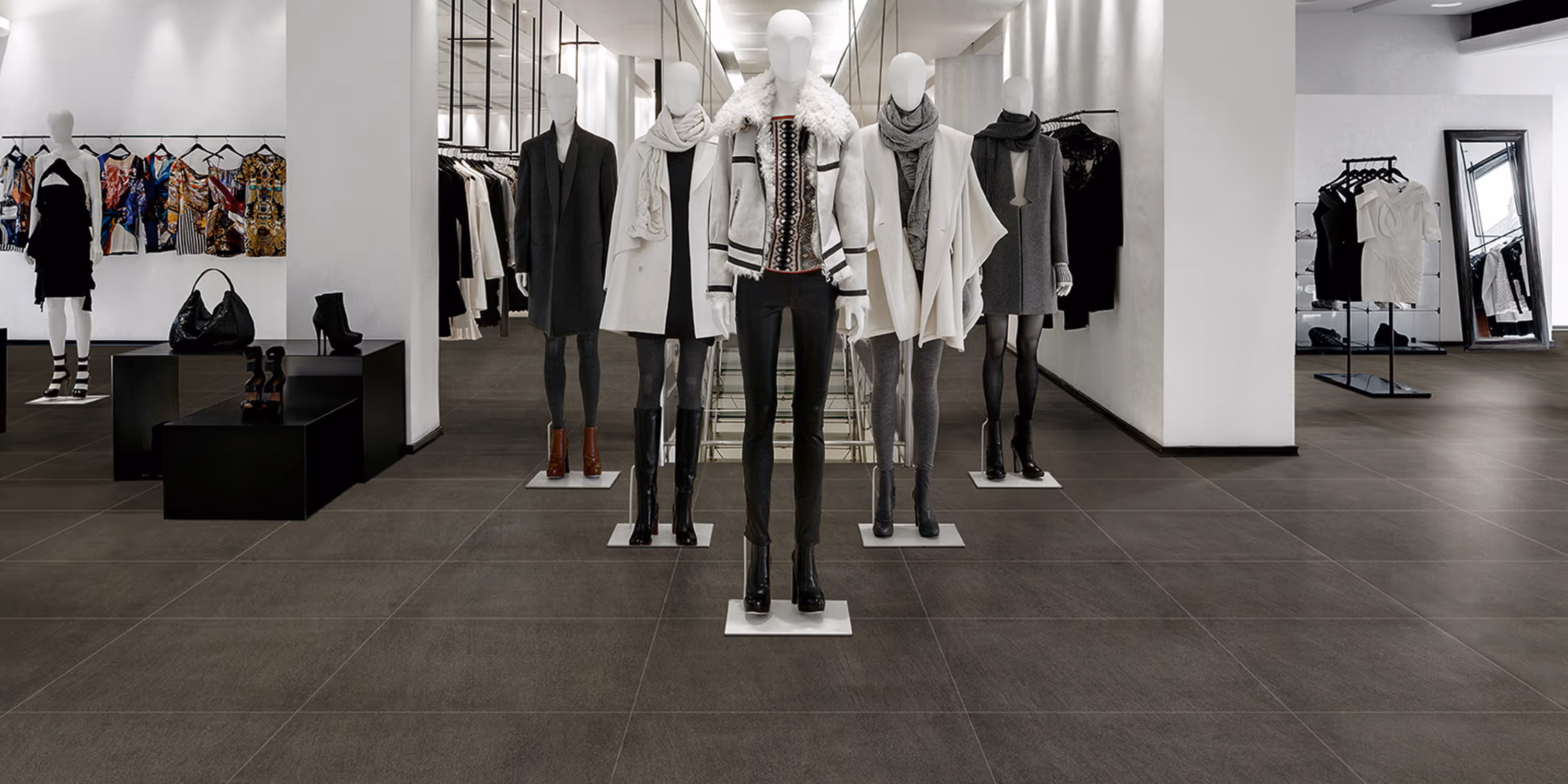 Fashion store interior with mannequins dressed in coats, scarves, and boots on dark tiled floor.