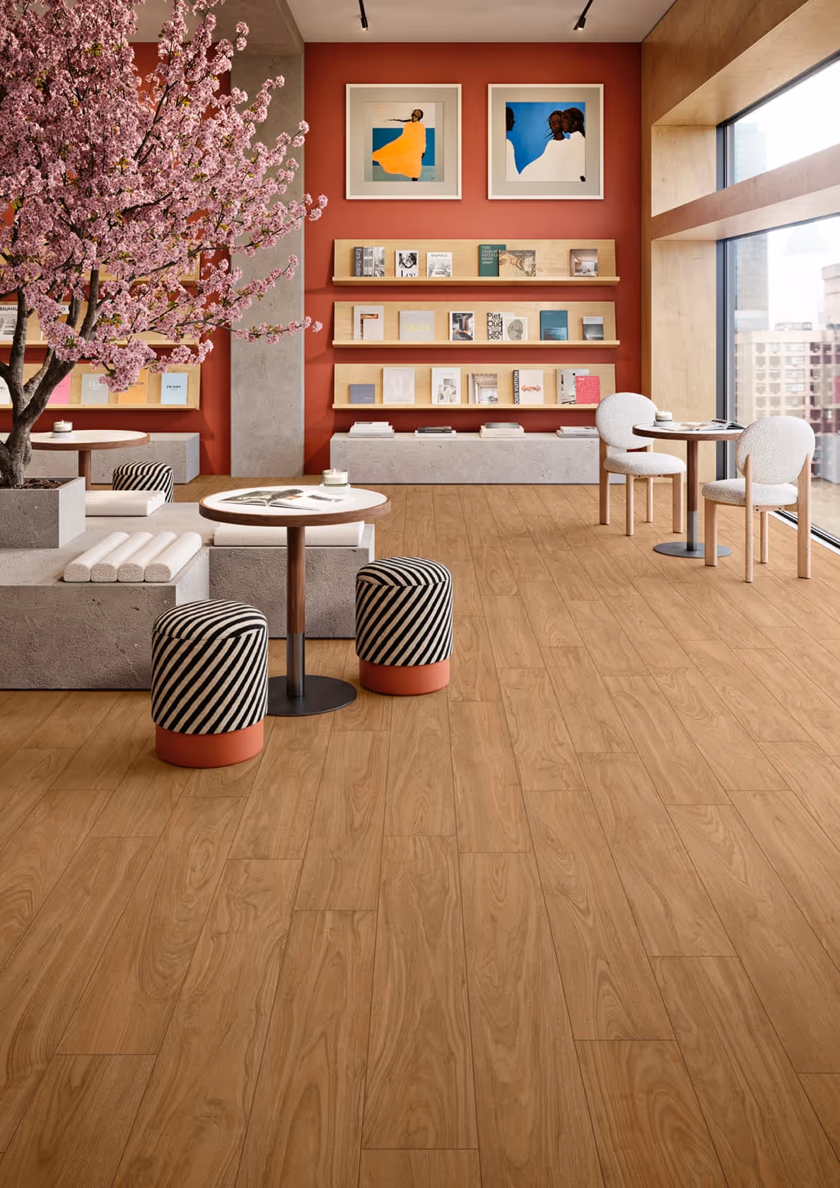 Modern seating area with wooden floor, pink flowered tree, small tables, shelves, and large window view.