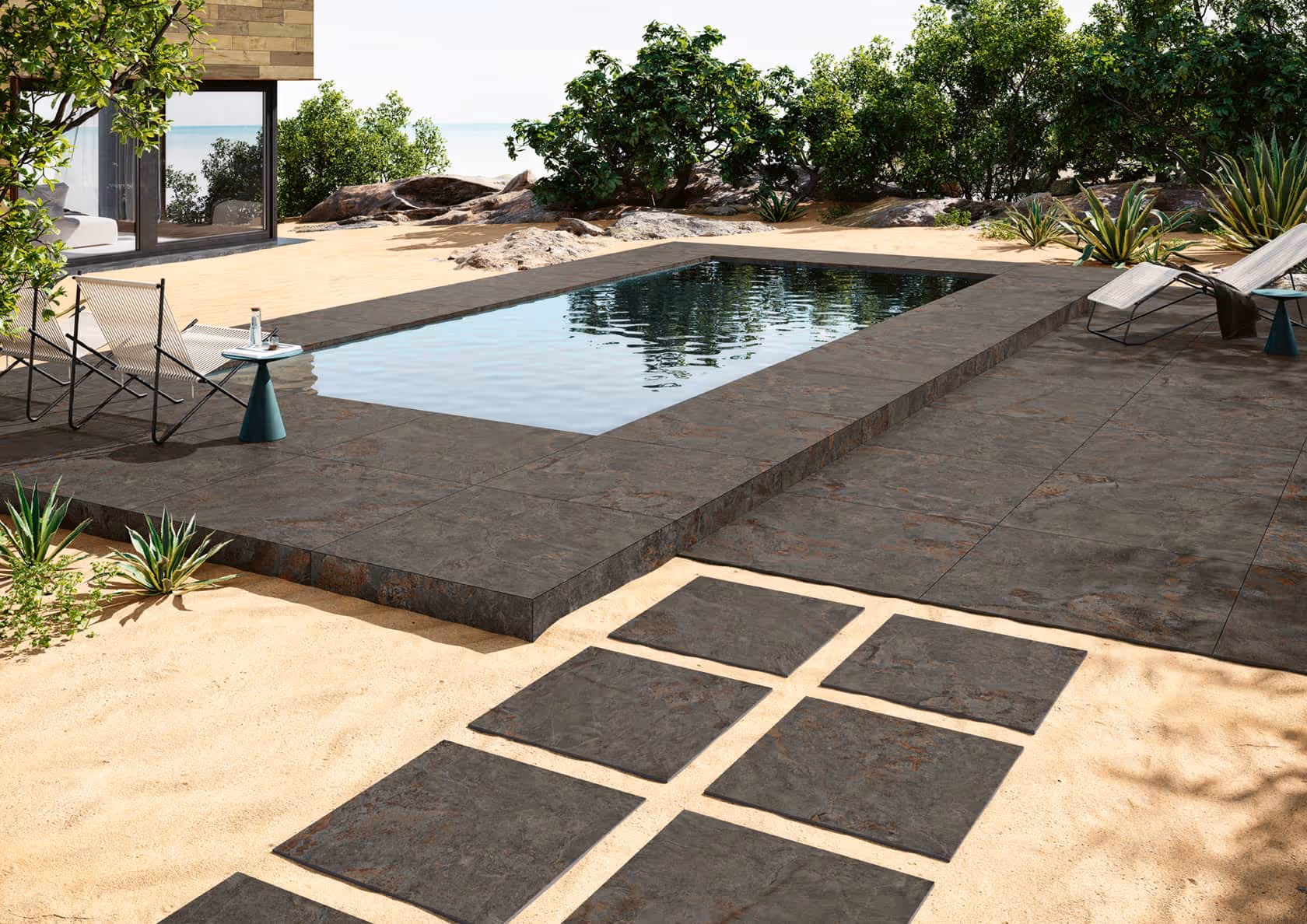 Modern backyard with rectangular pool, stone tiles, sandy ground, plants, and lounge chairs.