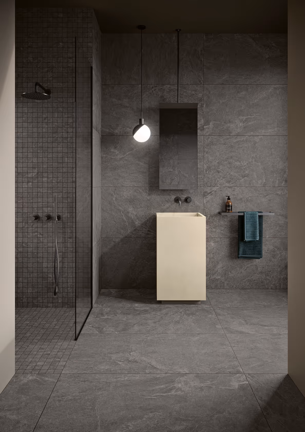 Modern bathroom with dark gray tiles, a beige pedestal sink, glass shower, round pendant light, and towels on a rack.