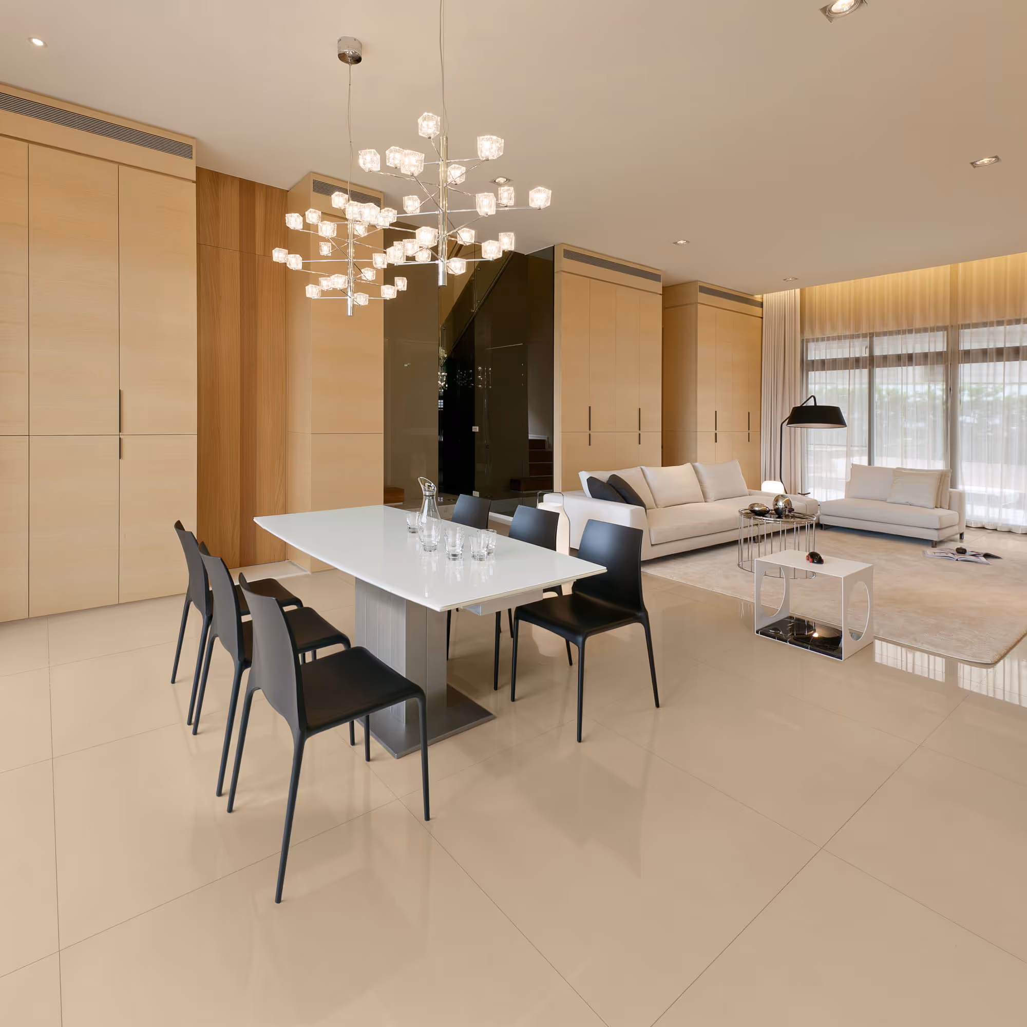 Modern open living and dining area with white table, black chairs, beige sofas, and large windows.