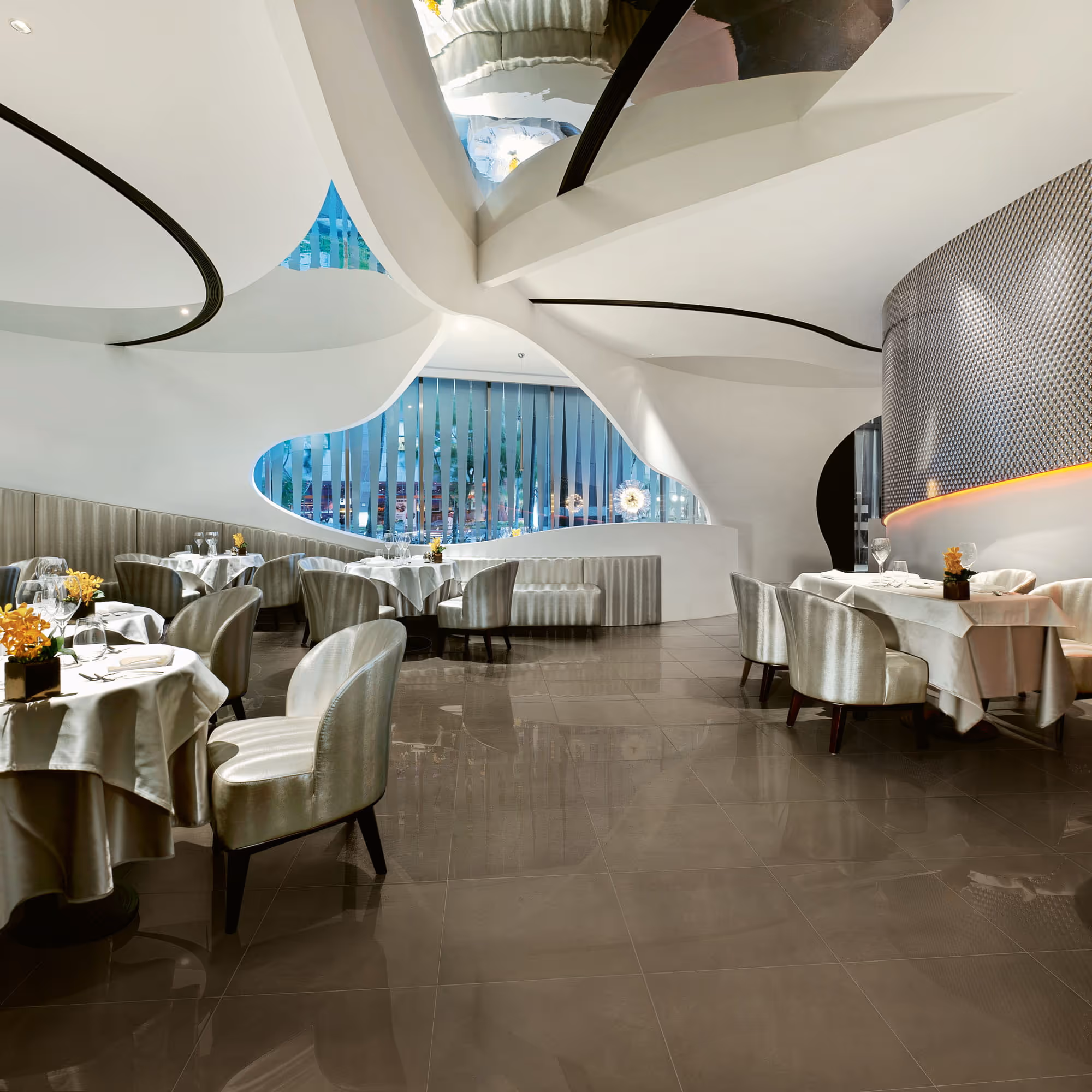 Modern fine dining restaurant with curved white ceilings, plush chairs, and tables set with white linens.