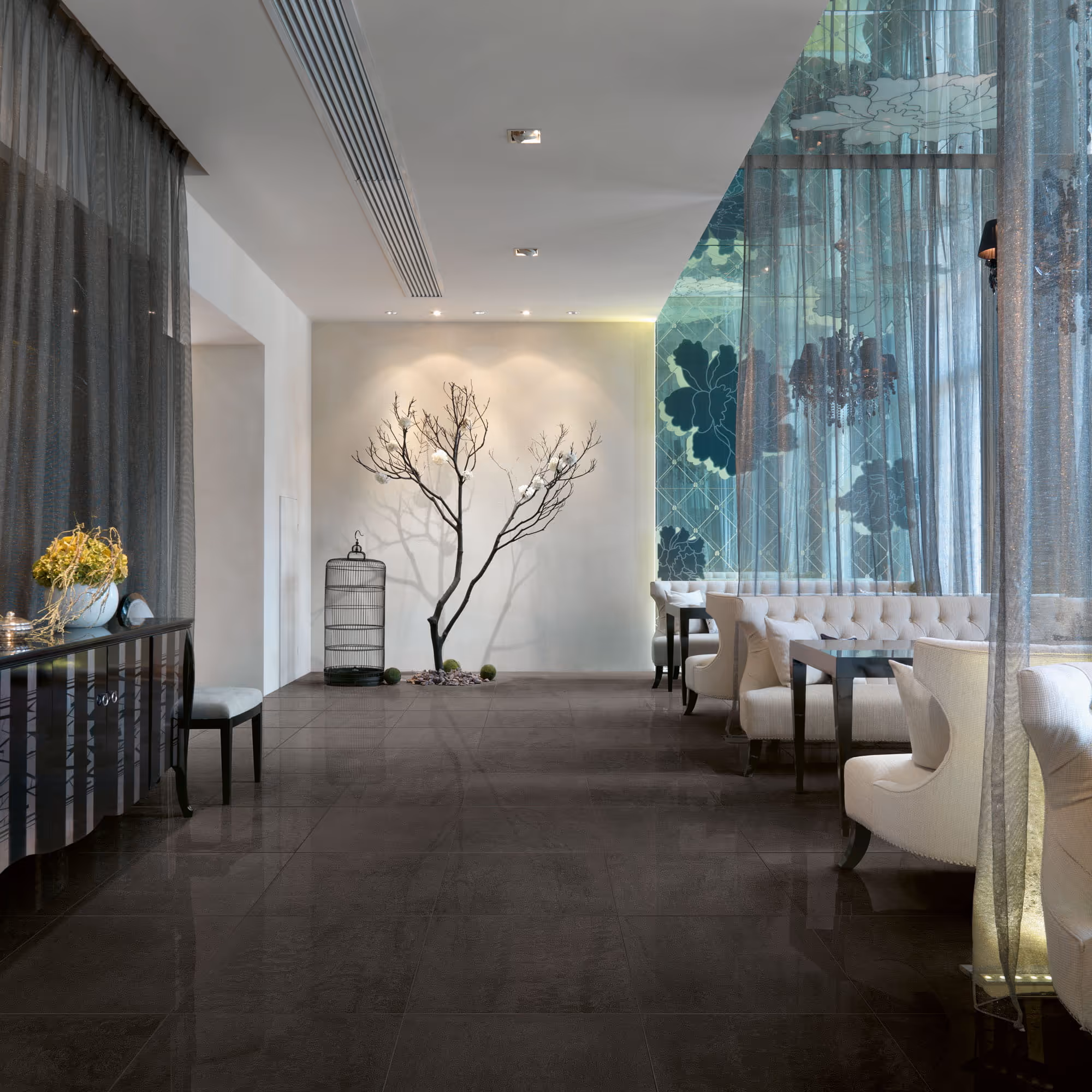 Modern seating area with white chairs, decorative tree, and patterned glass wall in a hotel lobby.