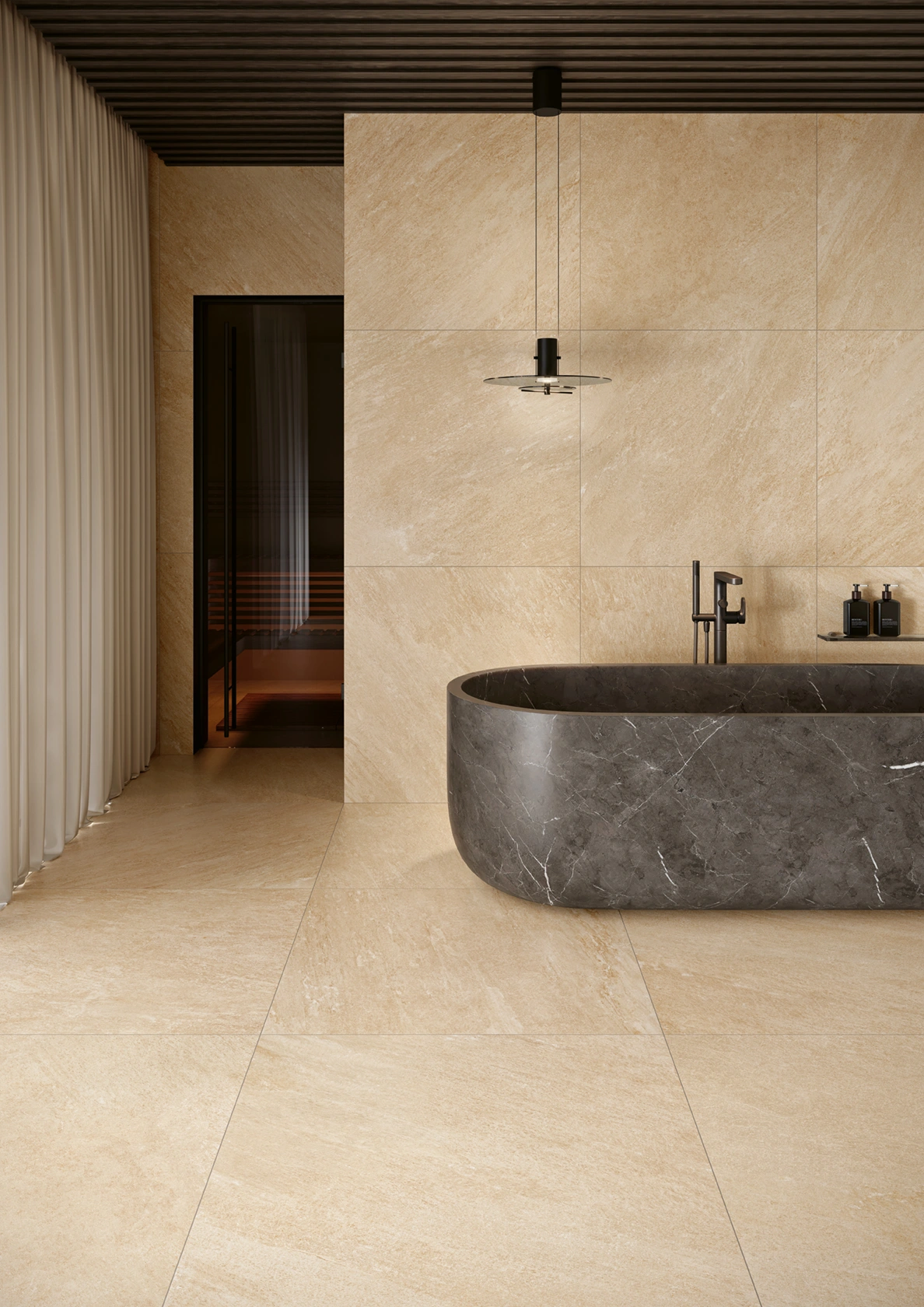Modern bathroom with beige stone tiles, dark stone bathtub, black faucet, and hanging light fixture.