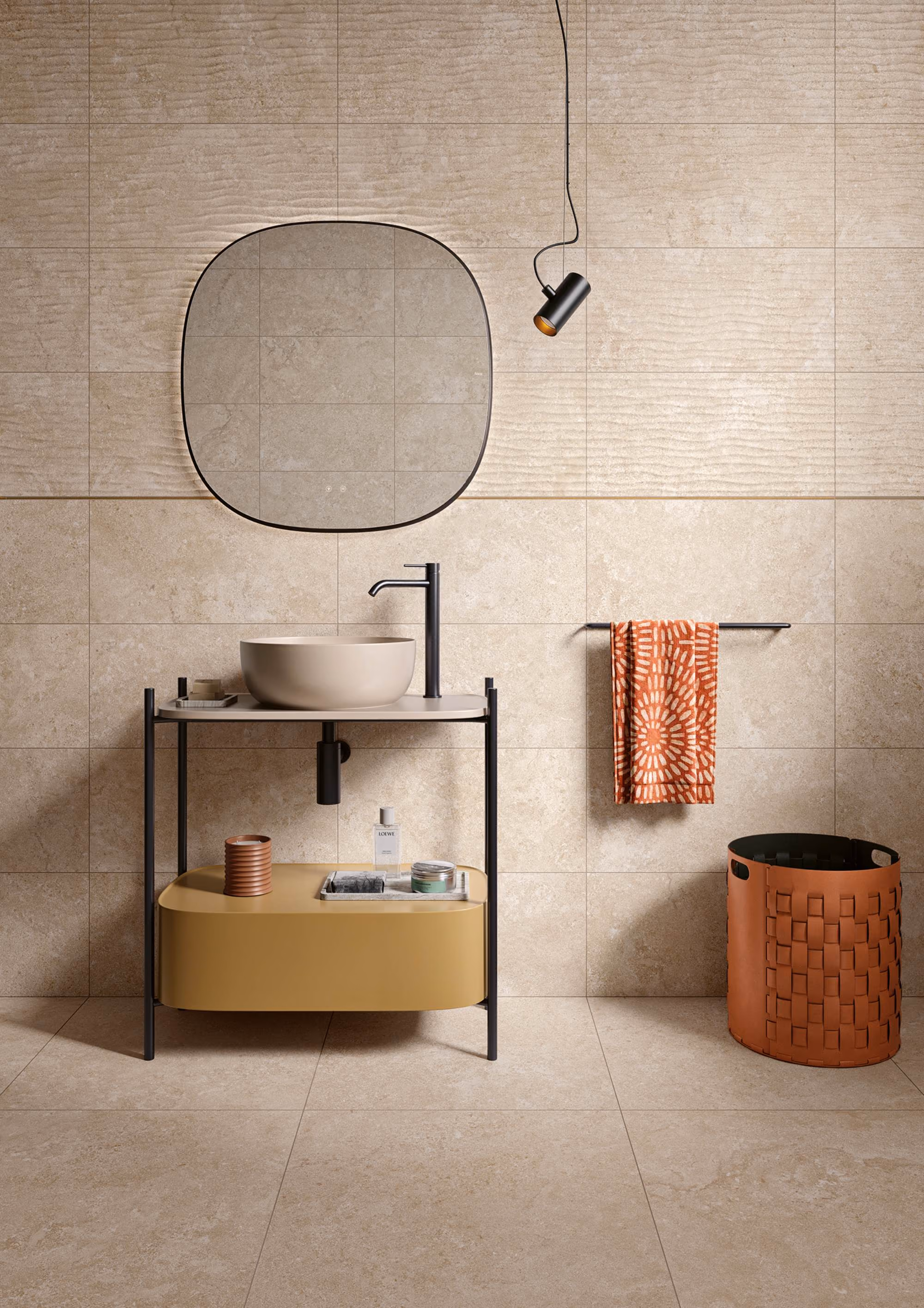 Modern bathroom with oval mirror, beige sink, black faucet, towel rack with orange towel, and woven basket.
