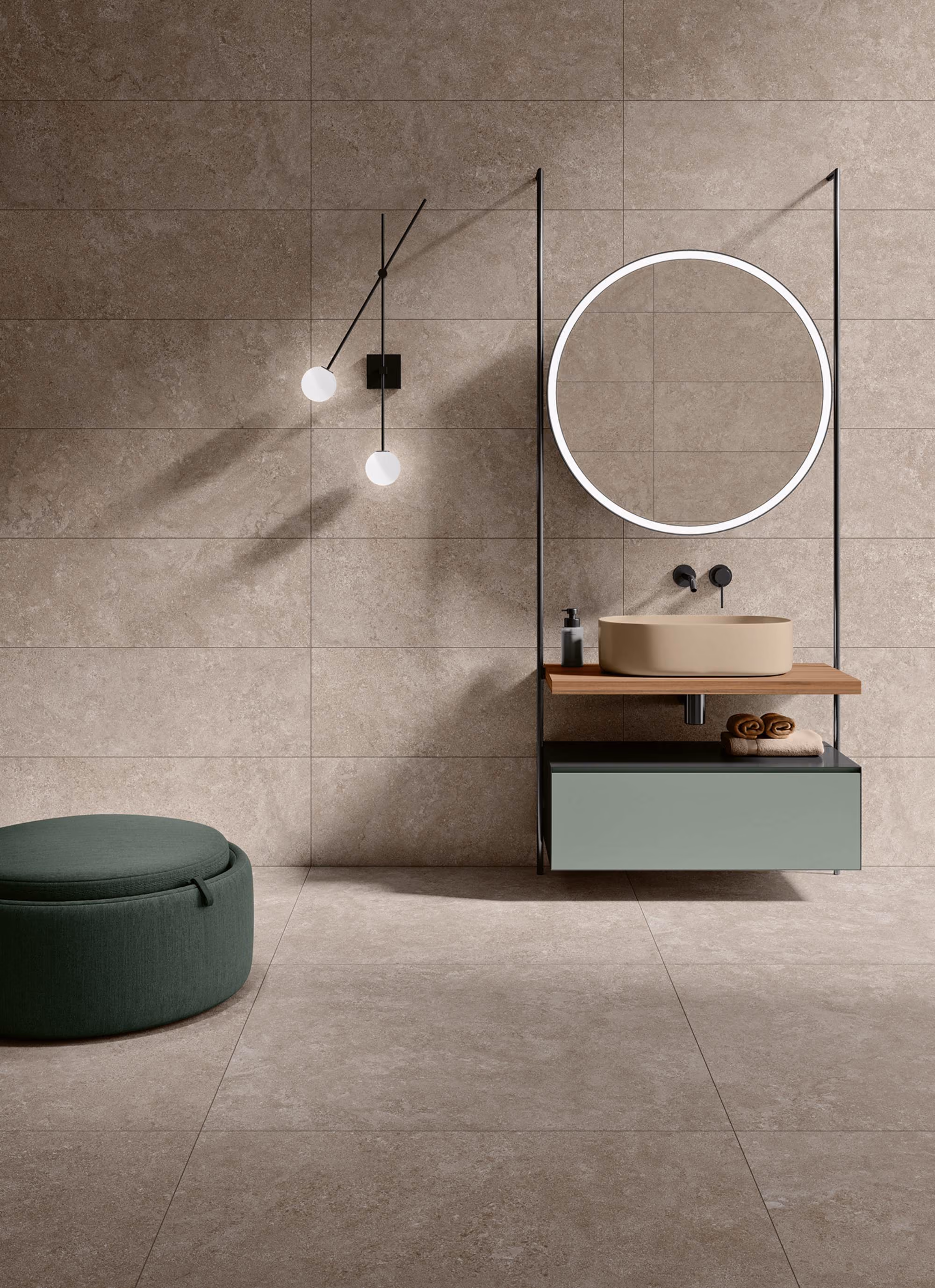 Minimalist bathroom with beige tiled walls, round mirror, beige sink, and green ottoman.