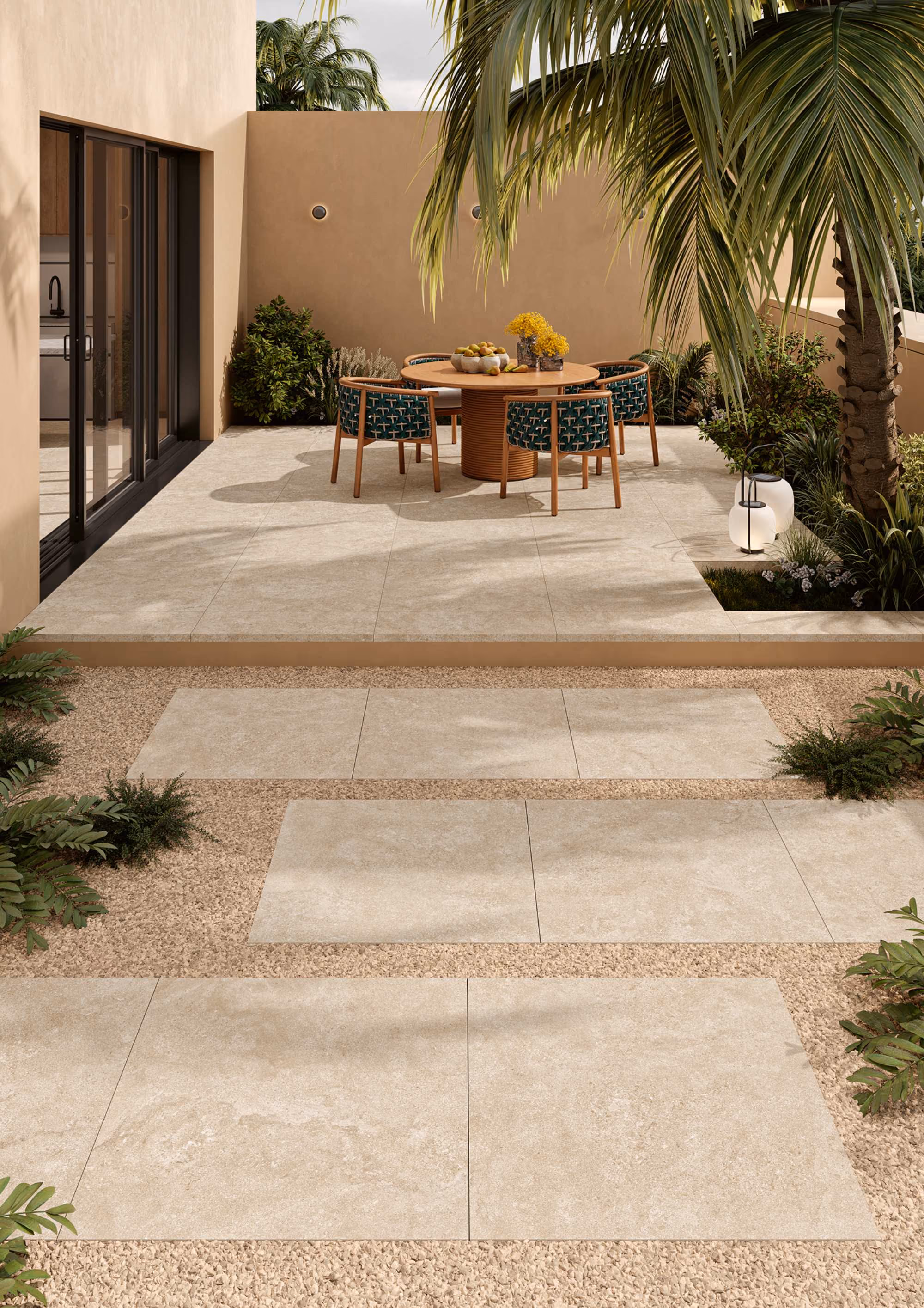 Outdoor patio with beige stone tiles, round wooden table, patterned chairs, plants, and palm trees.