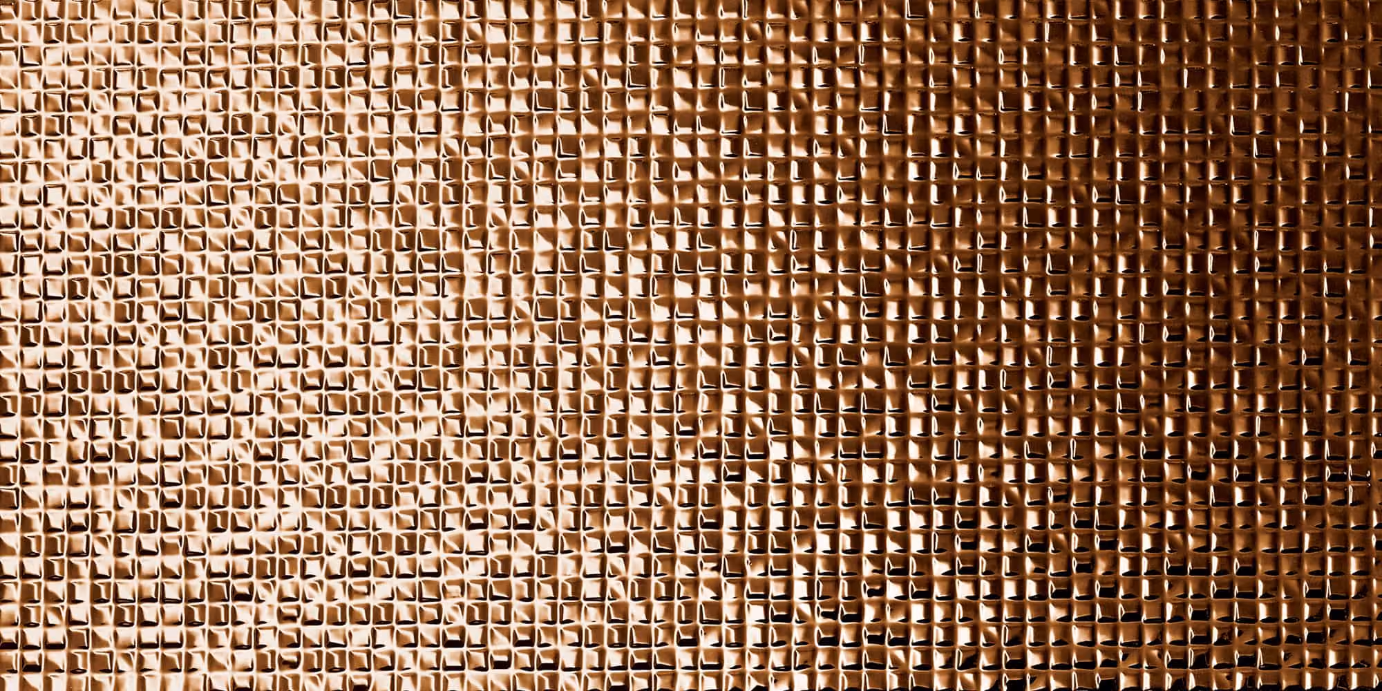 Close-up of textured copper surface with small raised squares reflecting light in warm tones.