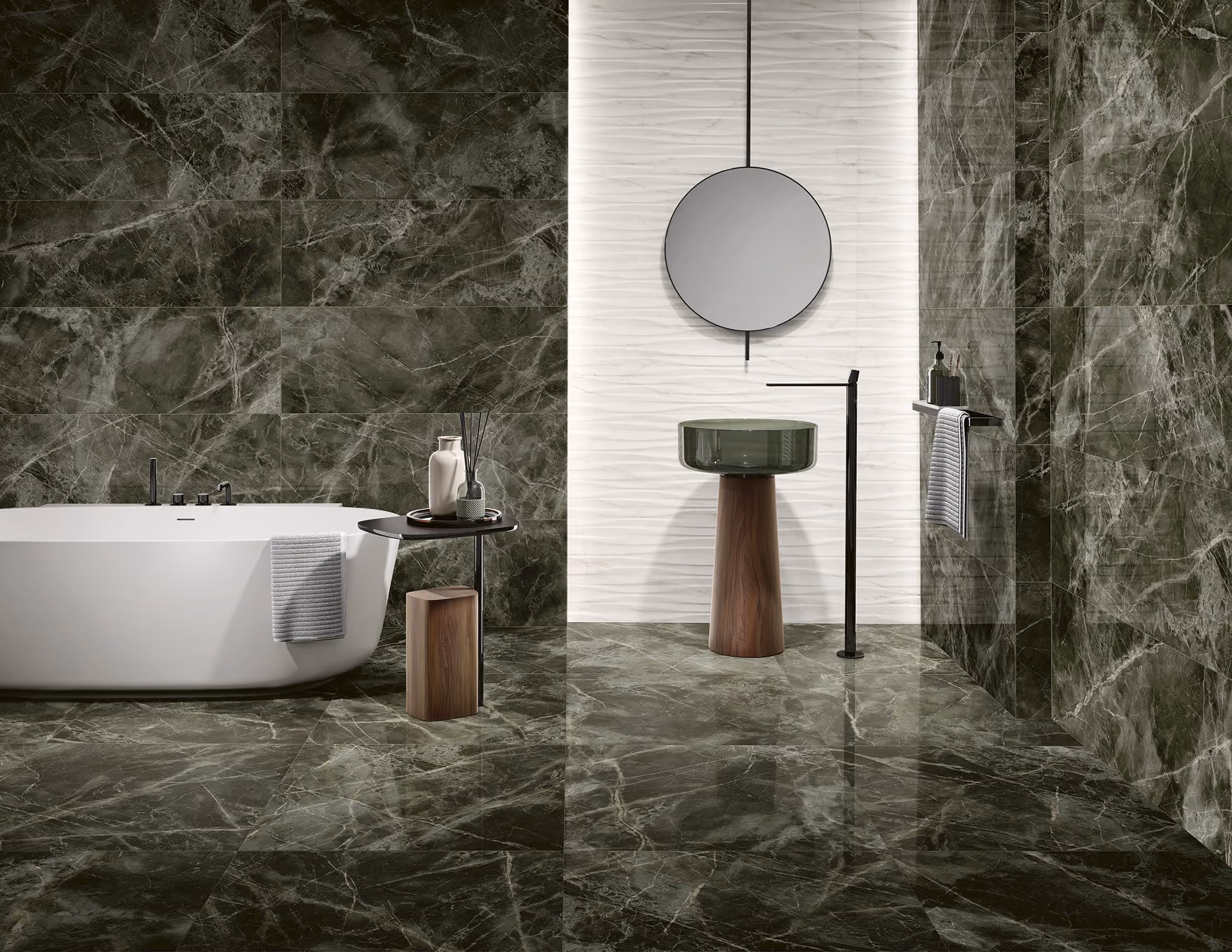Modern bathroom with dark marble floor and walls, a white bathtub, and a green glass sink with wooden base.