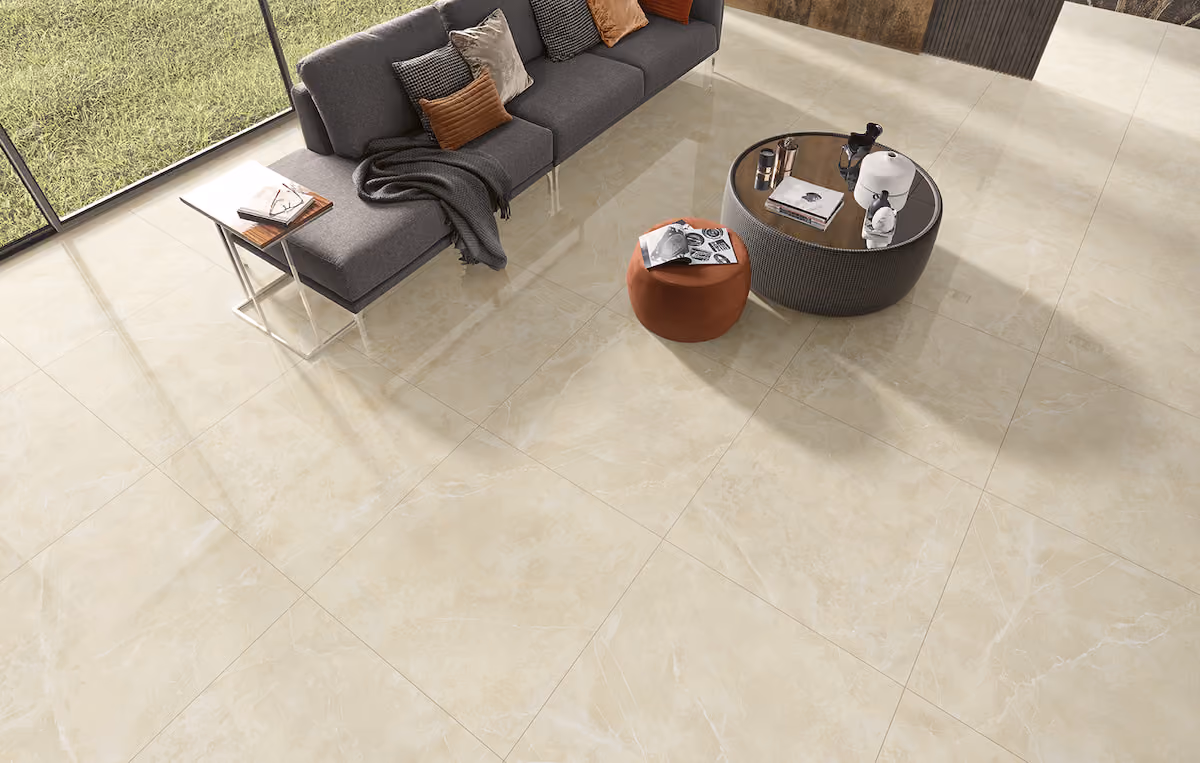 Living room with beige marble tile floor, gray sofa, round table, and orange ottoman.