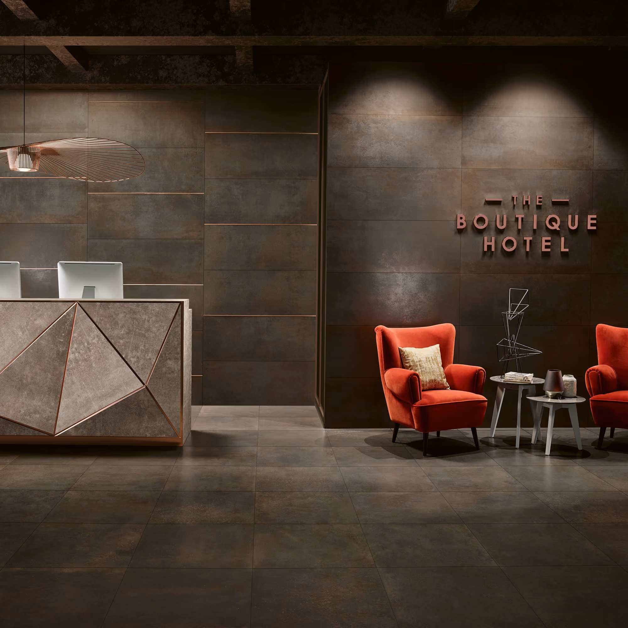 Modern hotel lobby with geometric reception desk, two red chairs, tables, and metallic sign reading The Boutique Hotel.