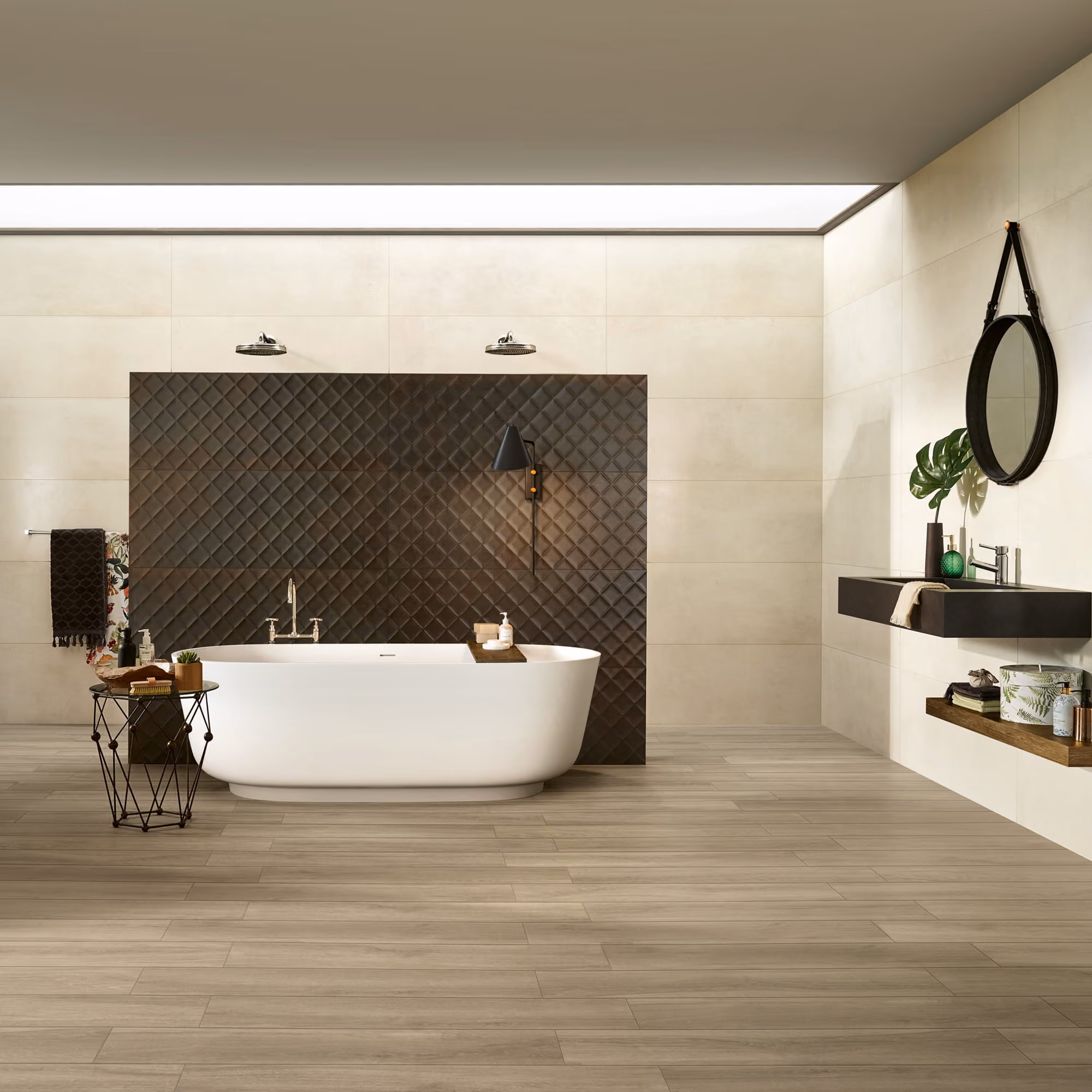 Modern bathroom with a white freestanding tub, dark tiled backsplash, round mirror, and wooden floor.
