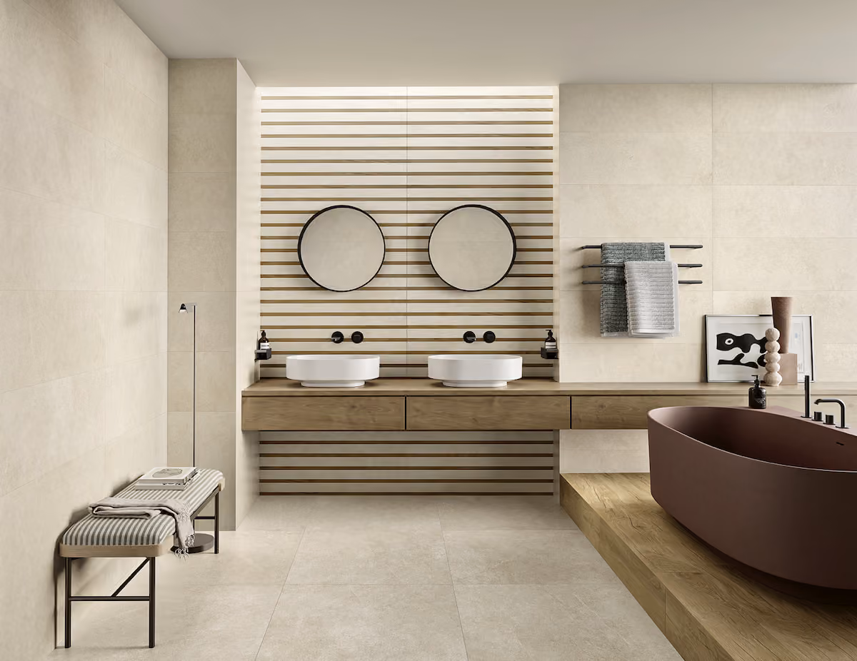 Modern bathroom with dual round mirrors, twin sinks, a brown bathtub, and a bench with towel.
