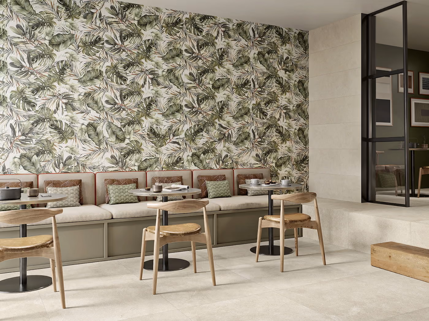 Modern seating area with wooden chairs, round tables, and a tropical leaf patterned wall behind a bench.