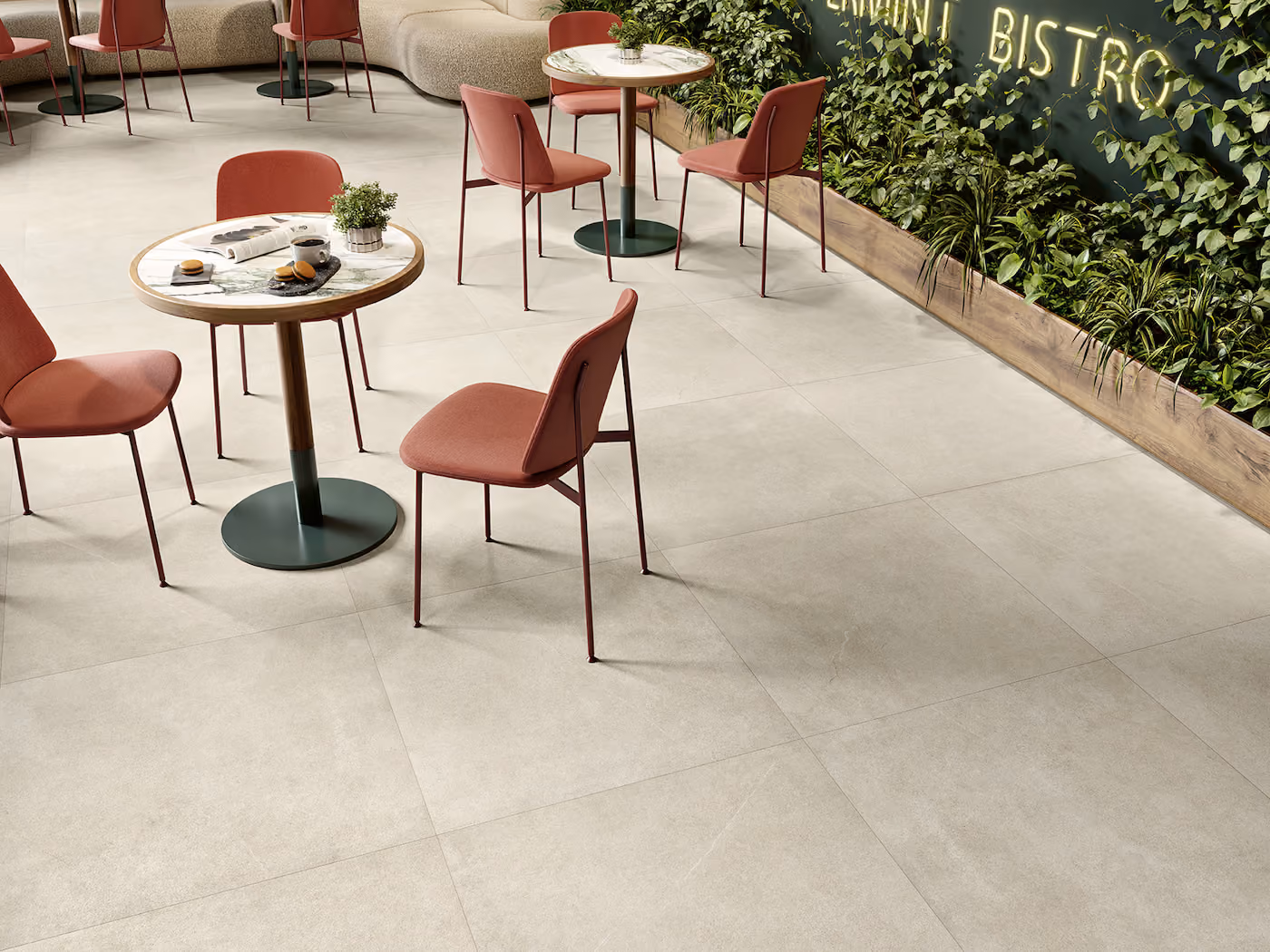 Modern bistro seating with round marble tables, pink chairs, and a green plant wall sign.