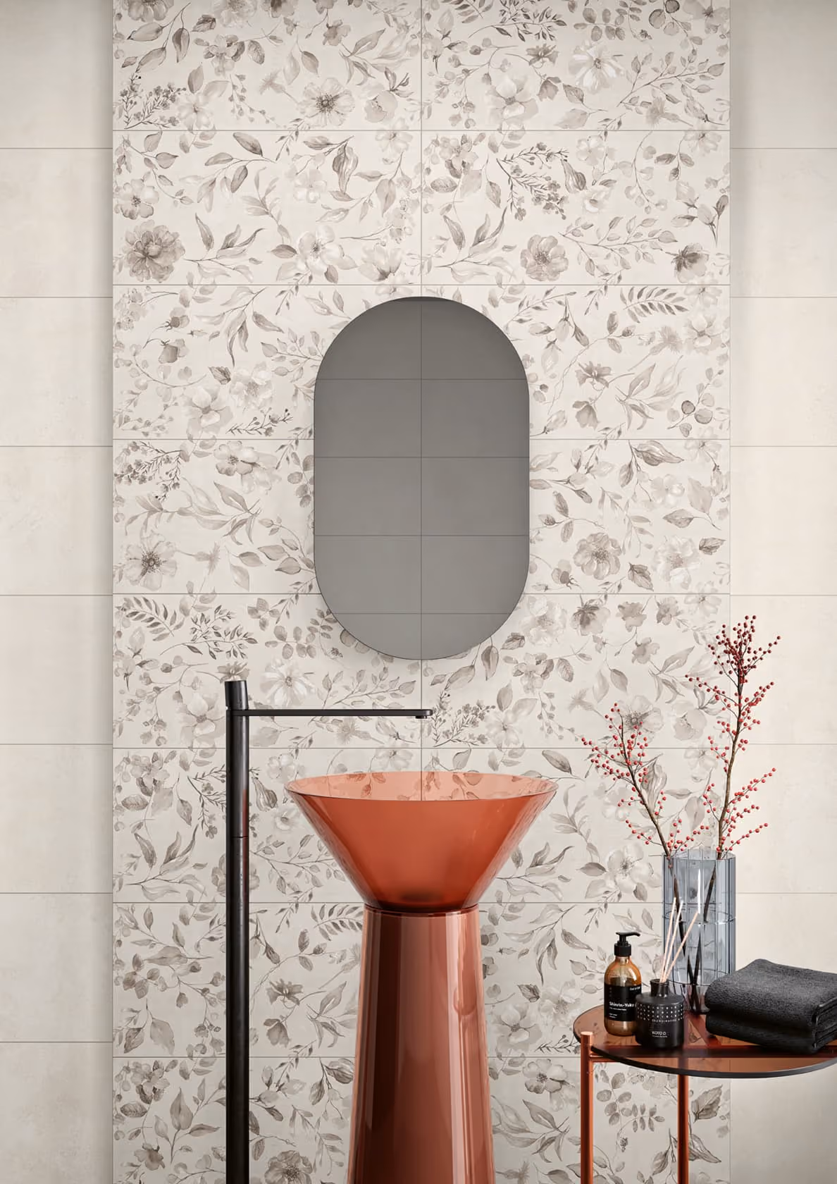 Modern bathroom with copper pedestal sink, black faucet, floral tiles, oval mirror, and side table with decor.