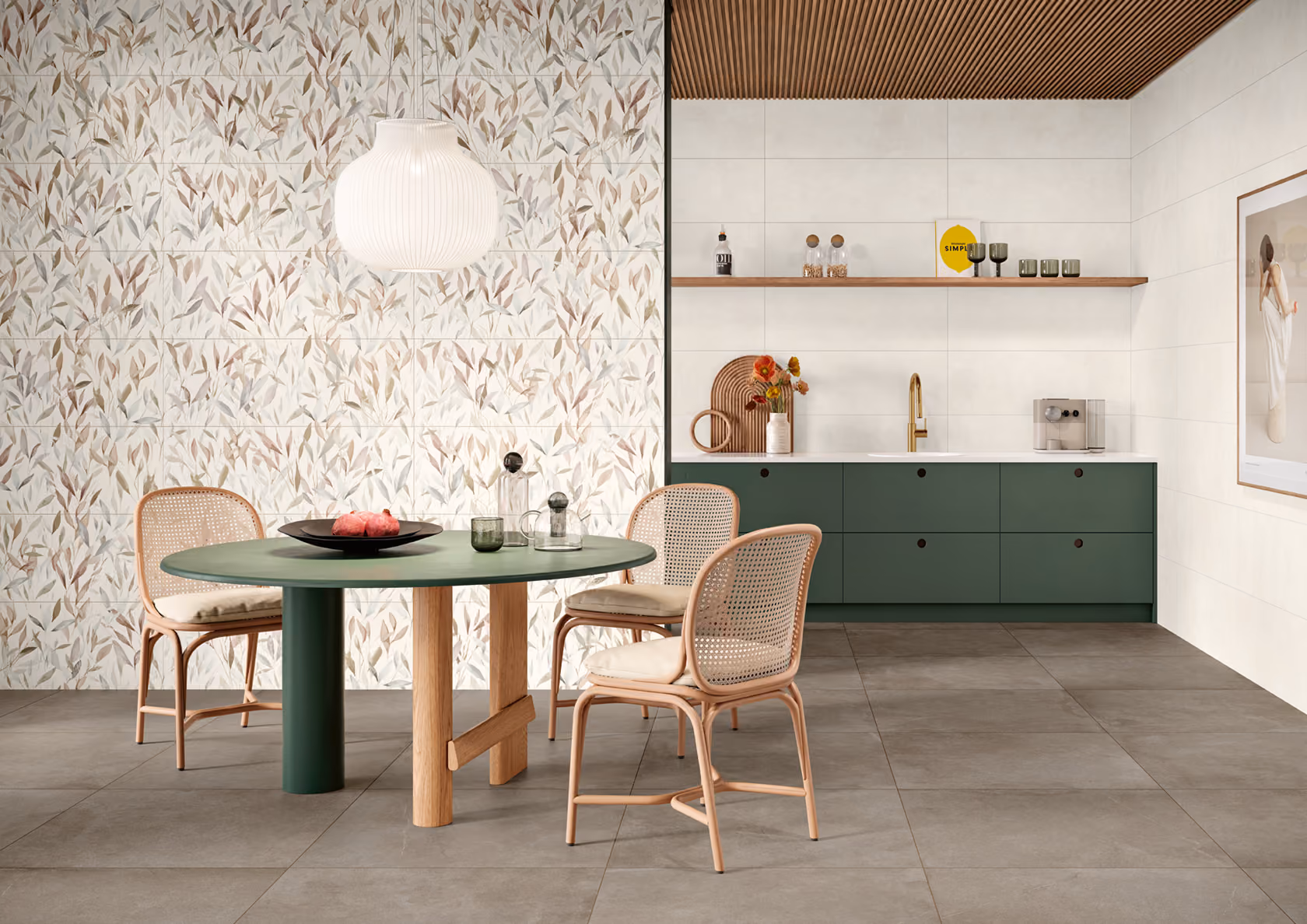 Modern dining area with green oval table, three wicker chairs, floral tiled wall, and kitchen cabinet.