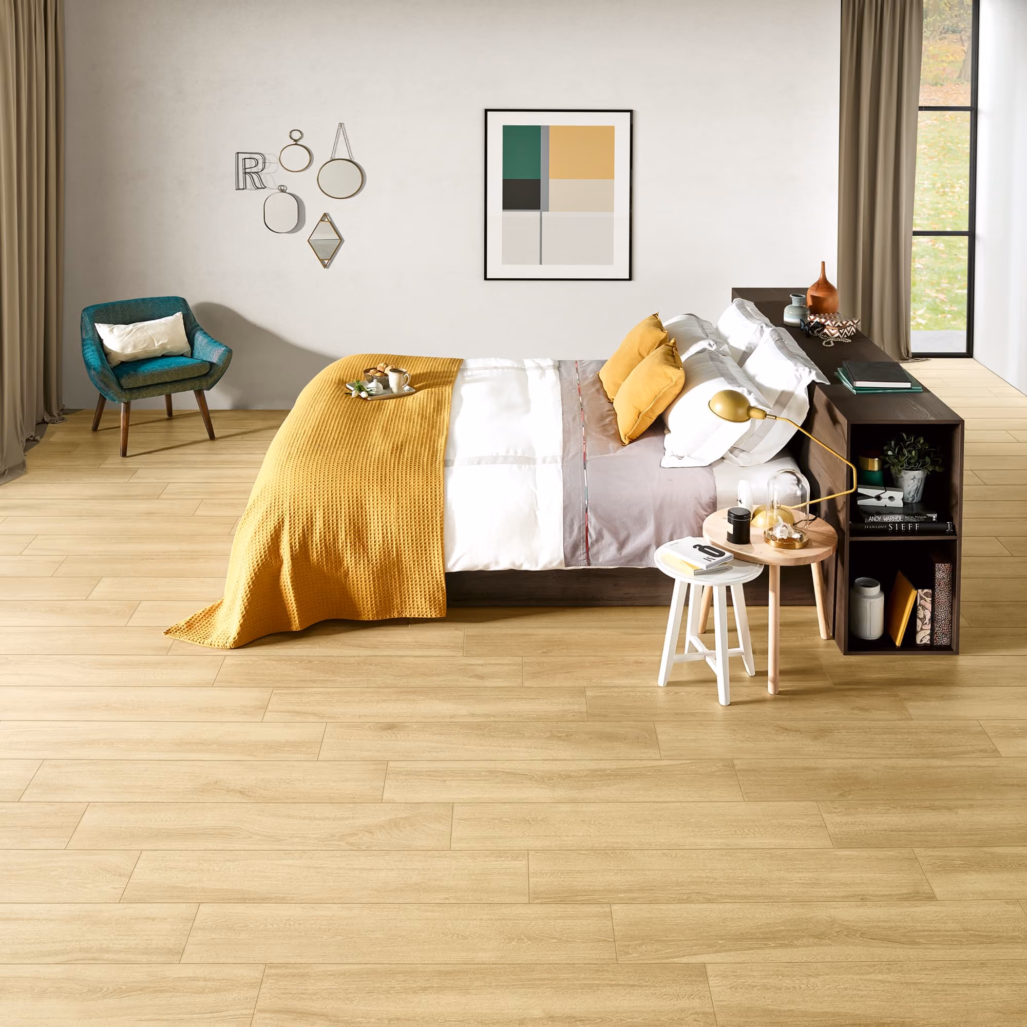 Modern bedroom with wooden floor, yellow blanket, teal chair, and minimalist wall art.