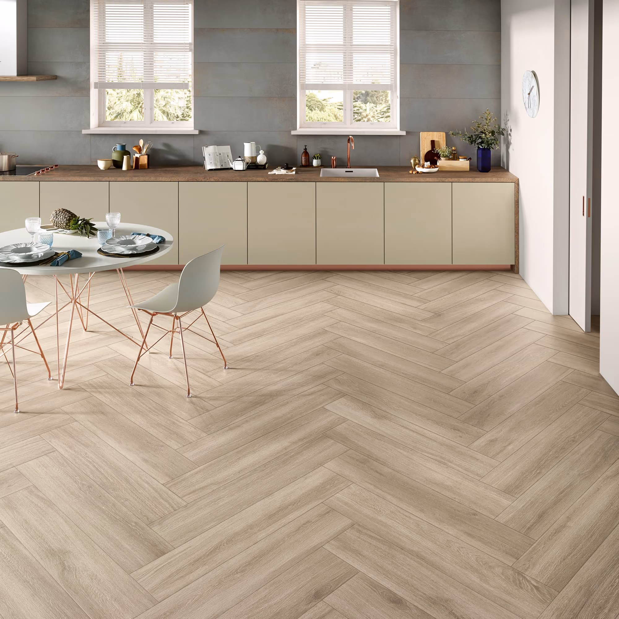 Modern kitchen with light wood herringbone floor, beige cabinets, round table set, and two windows.