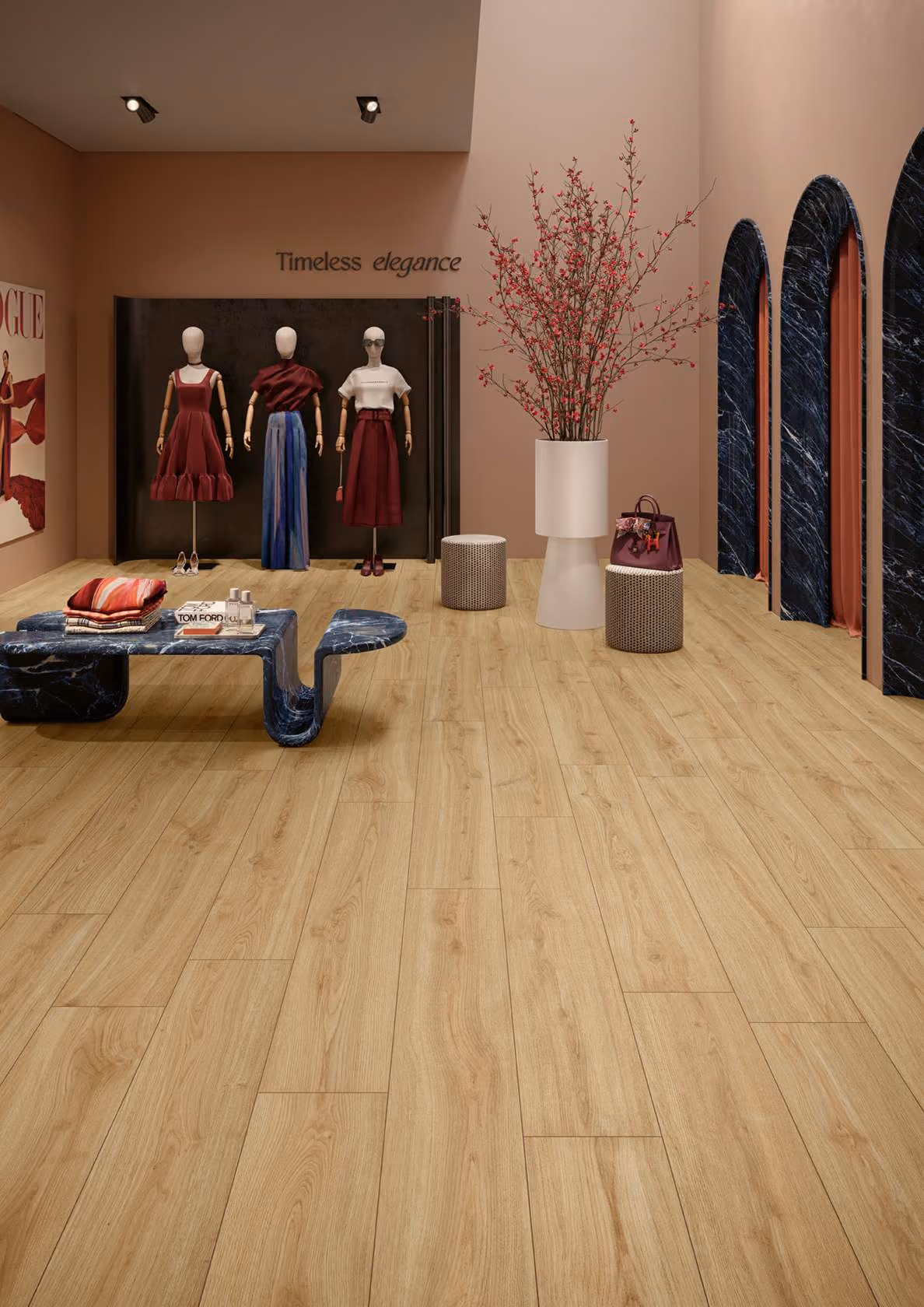 Fashion display with three mannequins, wooden floor, marble bench, and large vase with red flowers.