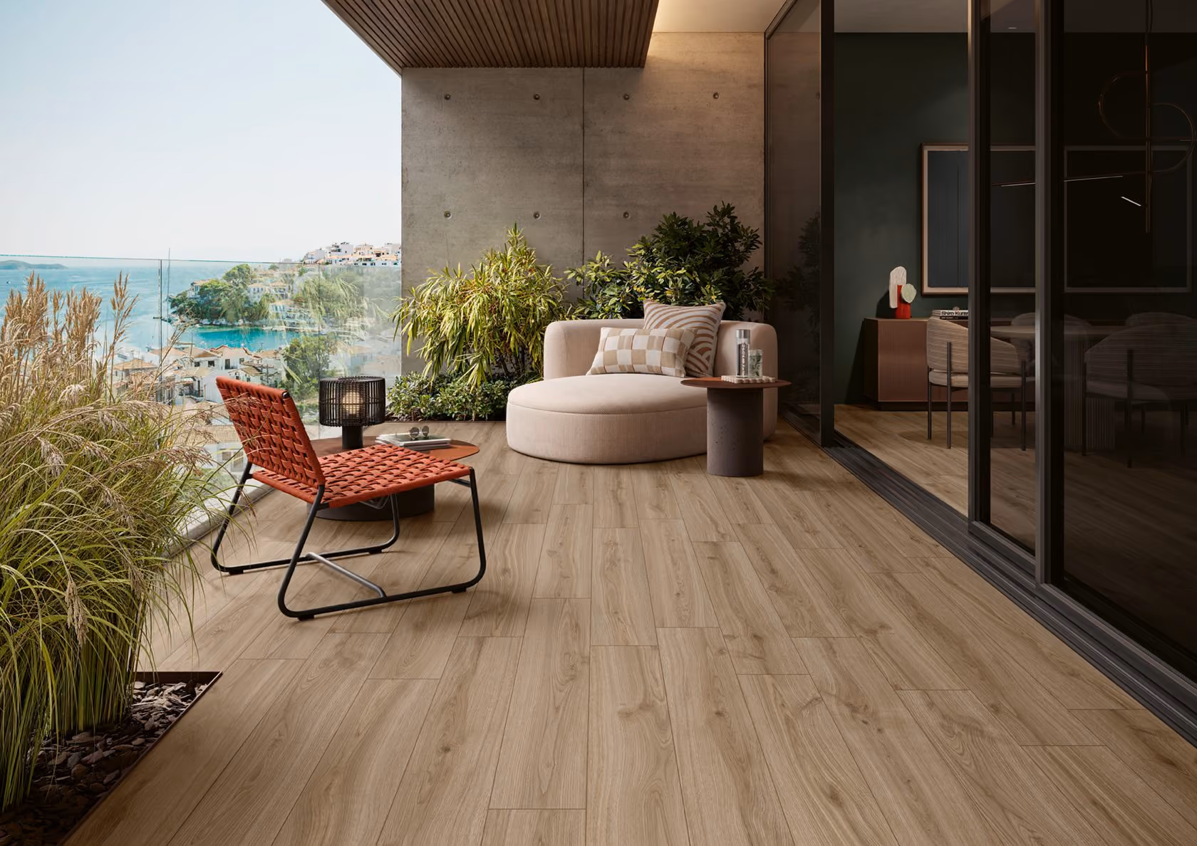 Modern balcony with light wood flooring, round beige chair, red woven chair, and sea view beyond glass railing.