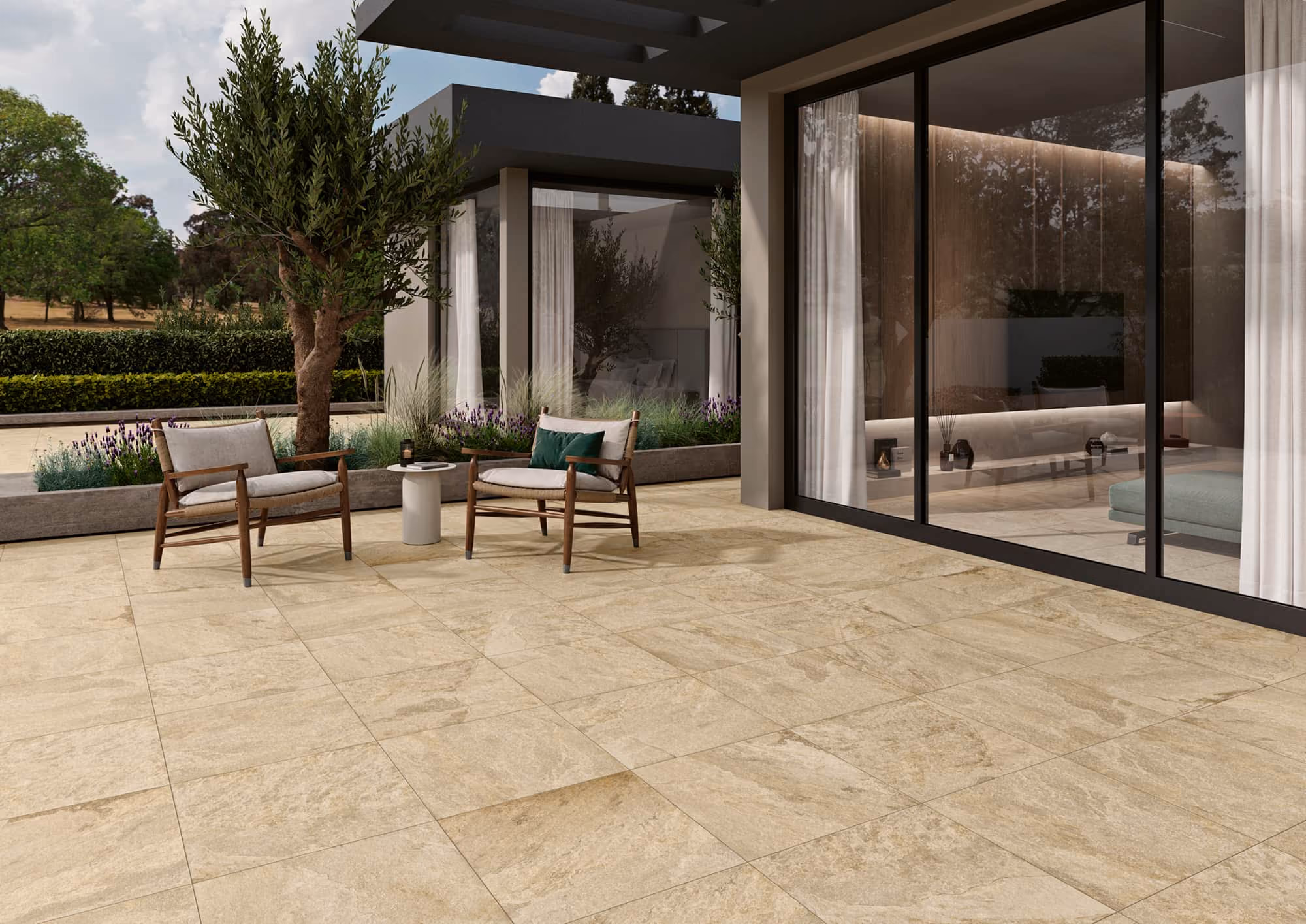 Outdoor patio with beige stone tiles, two wooden chairs, a small table, plants, and large glass doors.