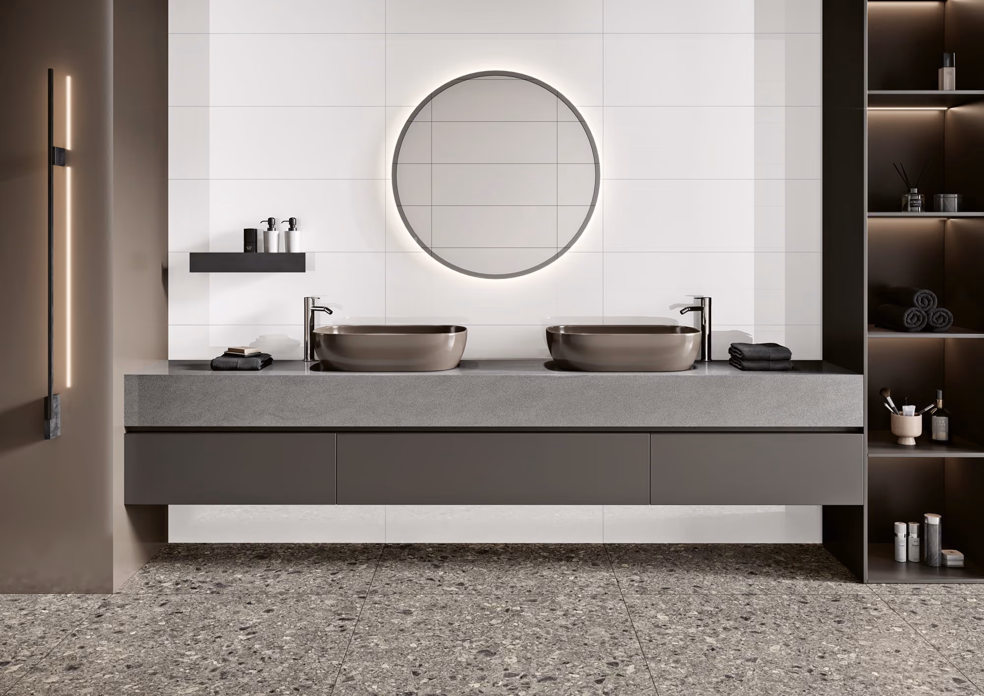 Modern bathroom with two gray vessel sinks, round backlit mirror, and open shelves with toiletries.