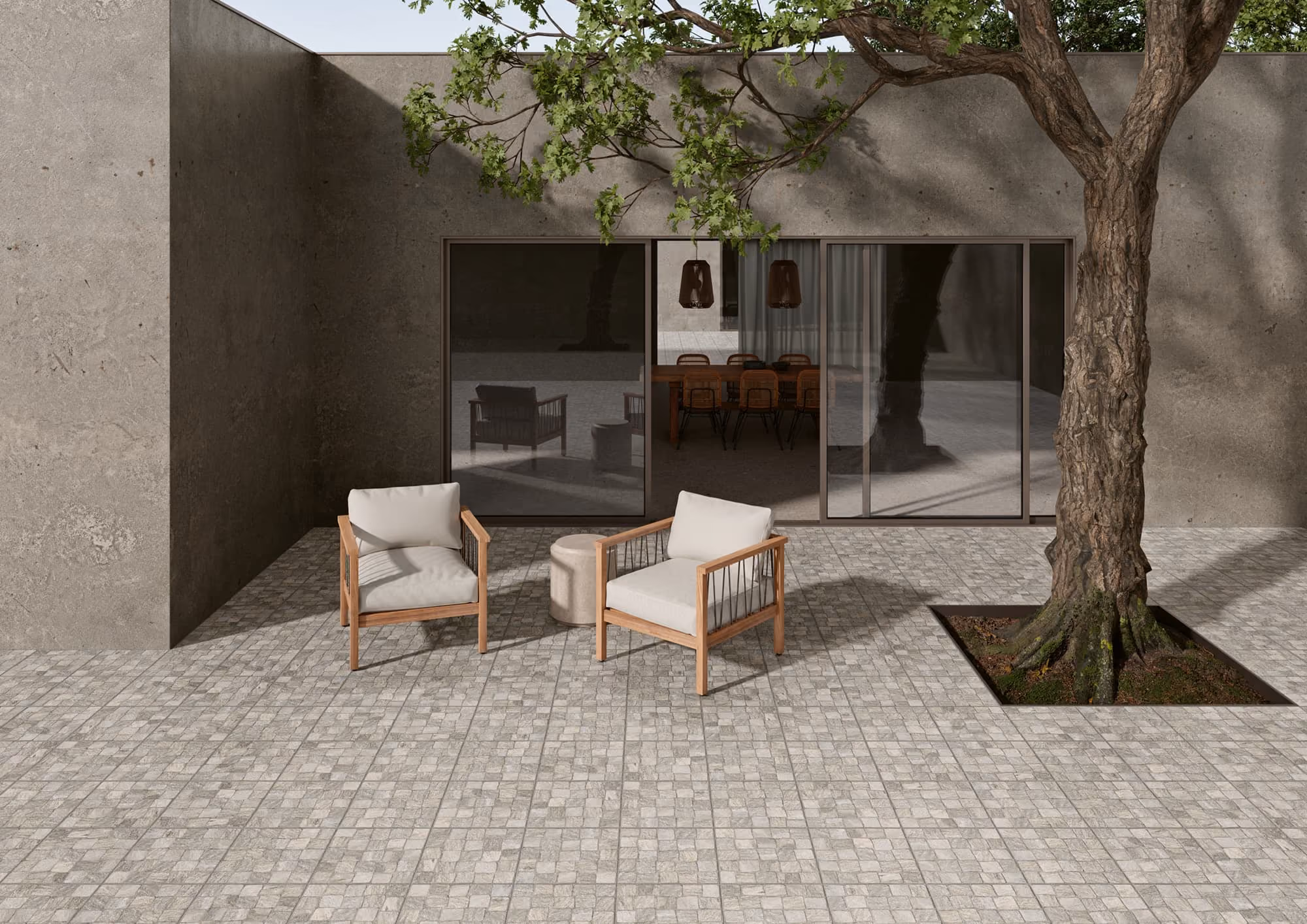 Minimalist patio with gray tiled floor, two wooden armchairs, round ottoman, and tree near a concrete wall.