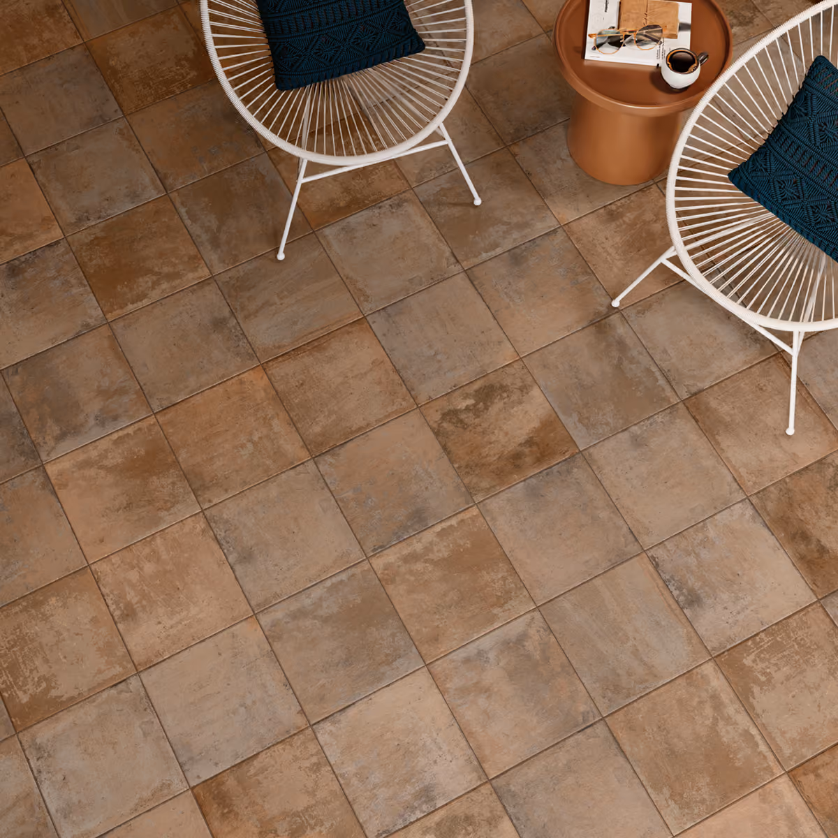 Top view of rustic brown square floor tiles with two white chairs and a round brown table.
