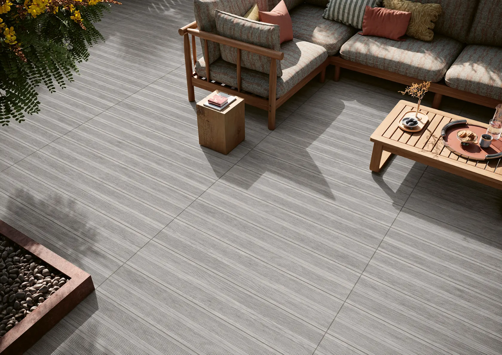 Modern outdoor patio with striped tile flooring, corner sofa with cushions, wooden side table and coffee table.