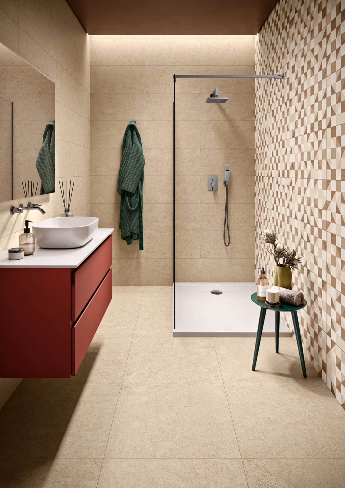 Modern bathroom with beige tiles, red vanity, green robe, walk-in shower, and small green side table.