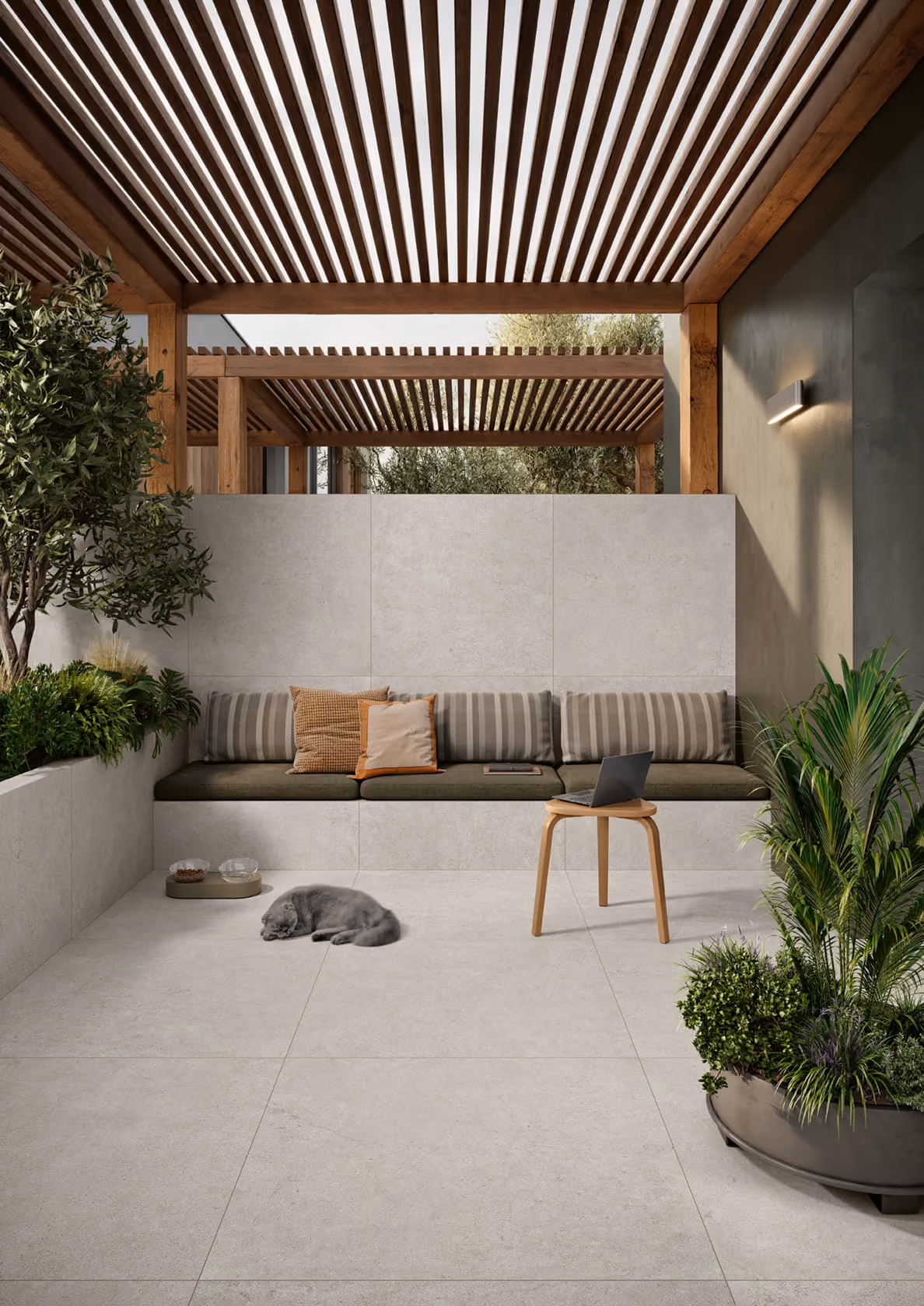 Modern outdoor patio with a wooden pergola, built-in bench, green cushions, plants, and a gray cat curled up.