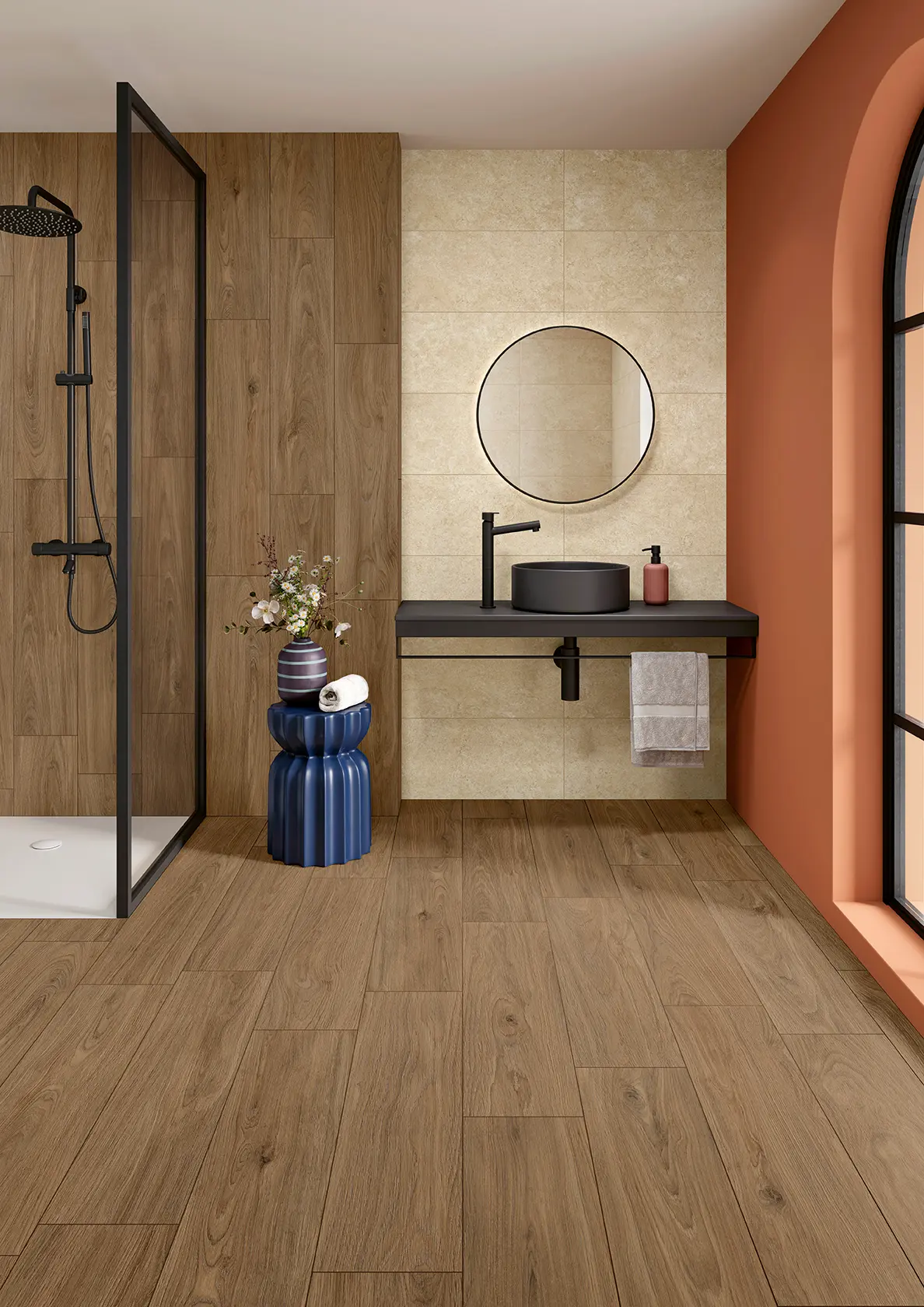 Modern bathroom with wood-style floor, black sink, round mirror, shower, and blue stool with flowers.